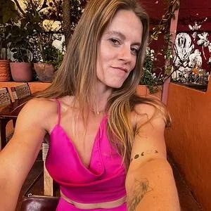 A woman with long red hair in a pink sleeveless top taking a selfie in a restaurant.