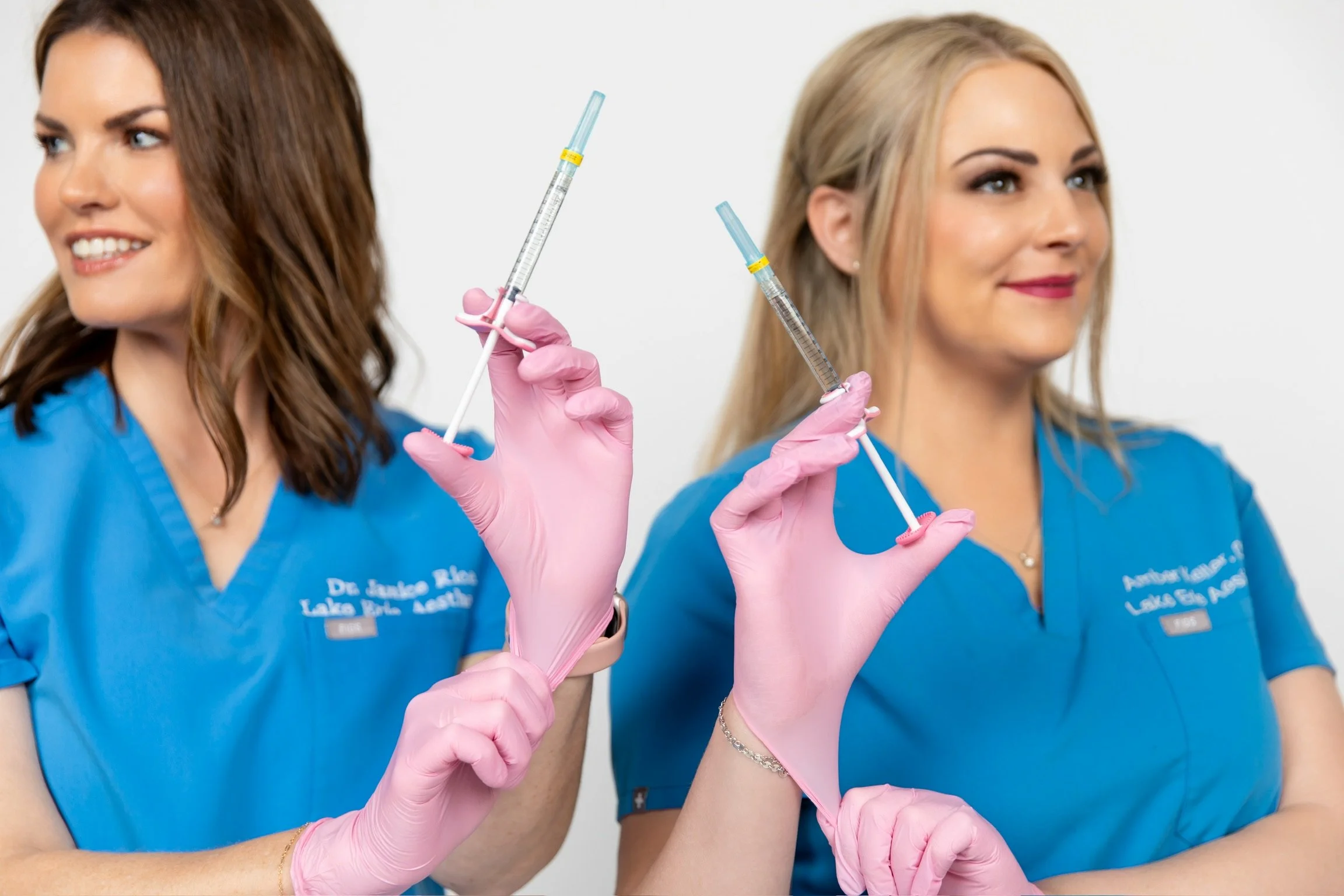 Two caucasian medical professionals in blue scrubs holding syringes close to one another