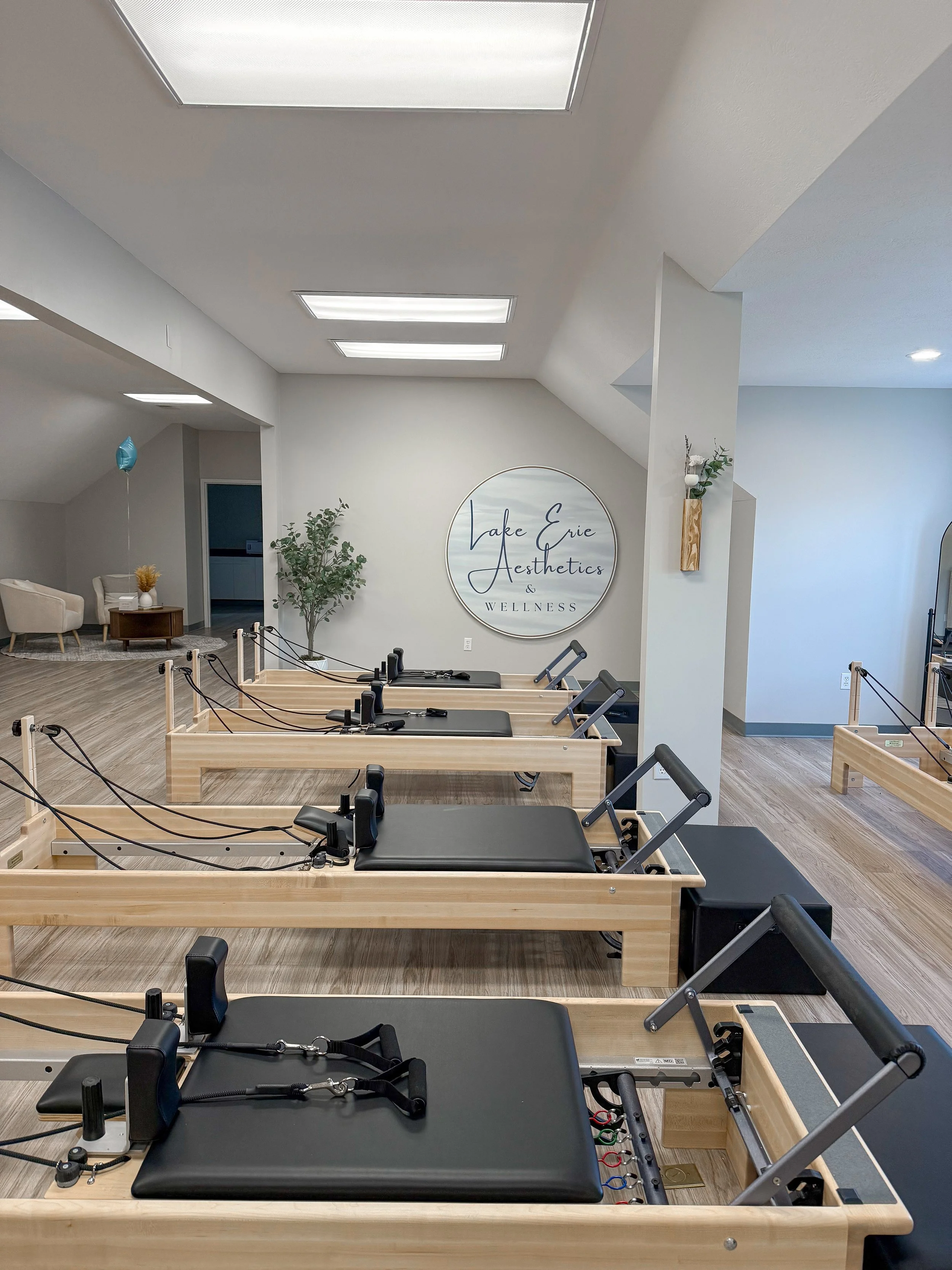 Pilates reformer machines in a wellness center called Lake Erie Aesthetics & Wellness with white walls, wooden floors, and modern decor.