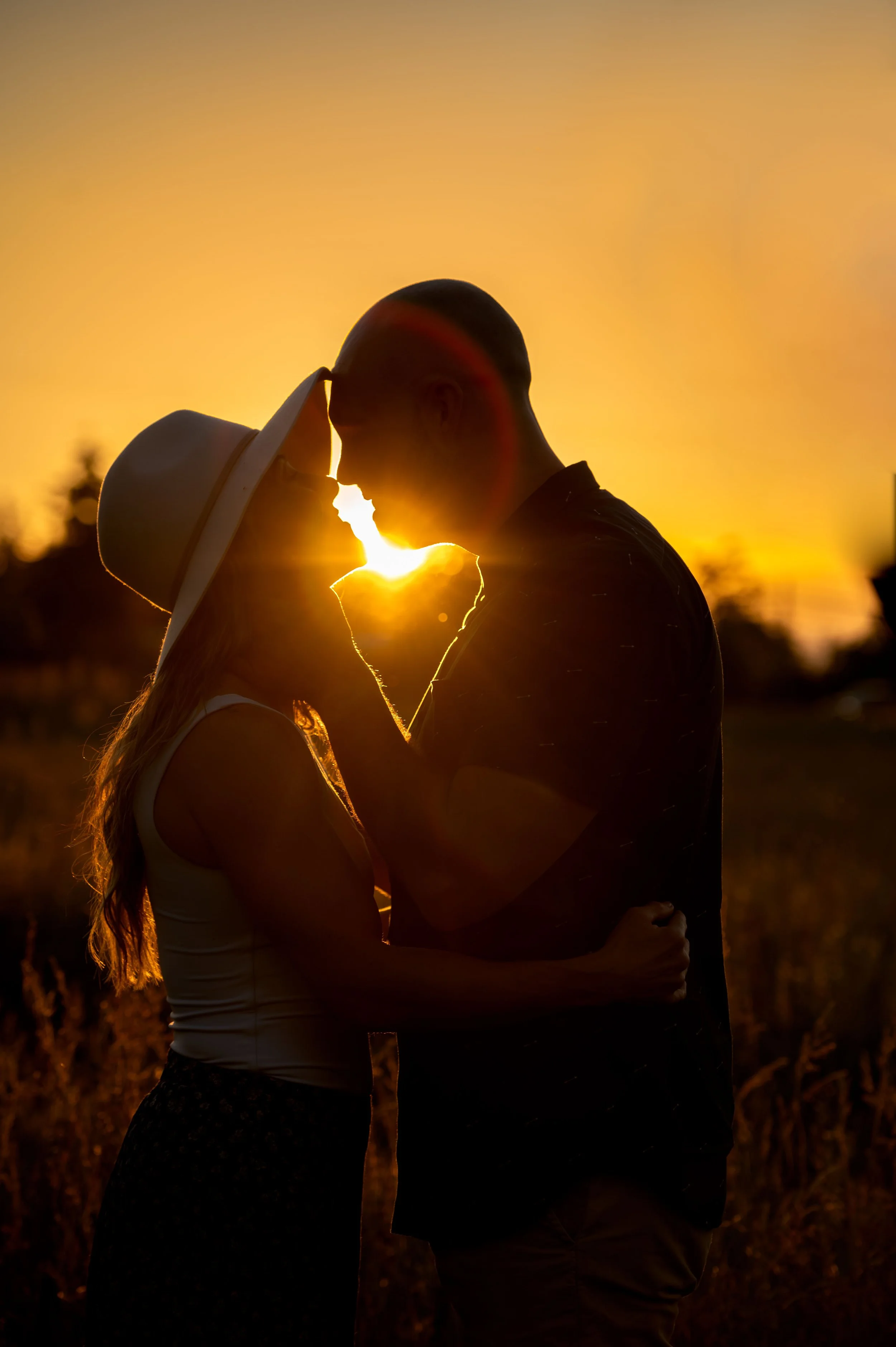 Silhouetted couple touching foreheads during sunset, with the sun shining between them.