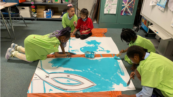 Step 3: This mural was painted on parachute paper. Parachute paper is a canvas-like material that is used as an alternative to painting murals directly on the wall. Here are students painting the individual sheets of parachute paper. 