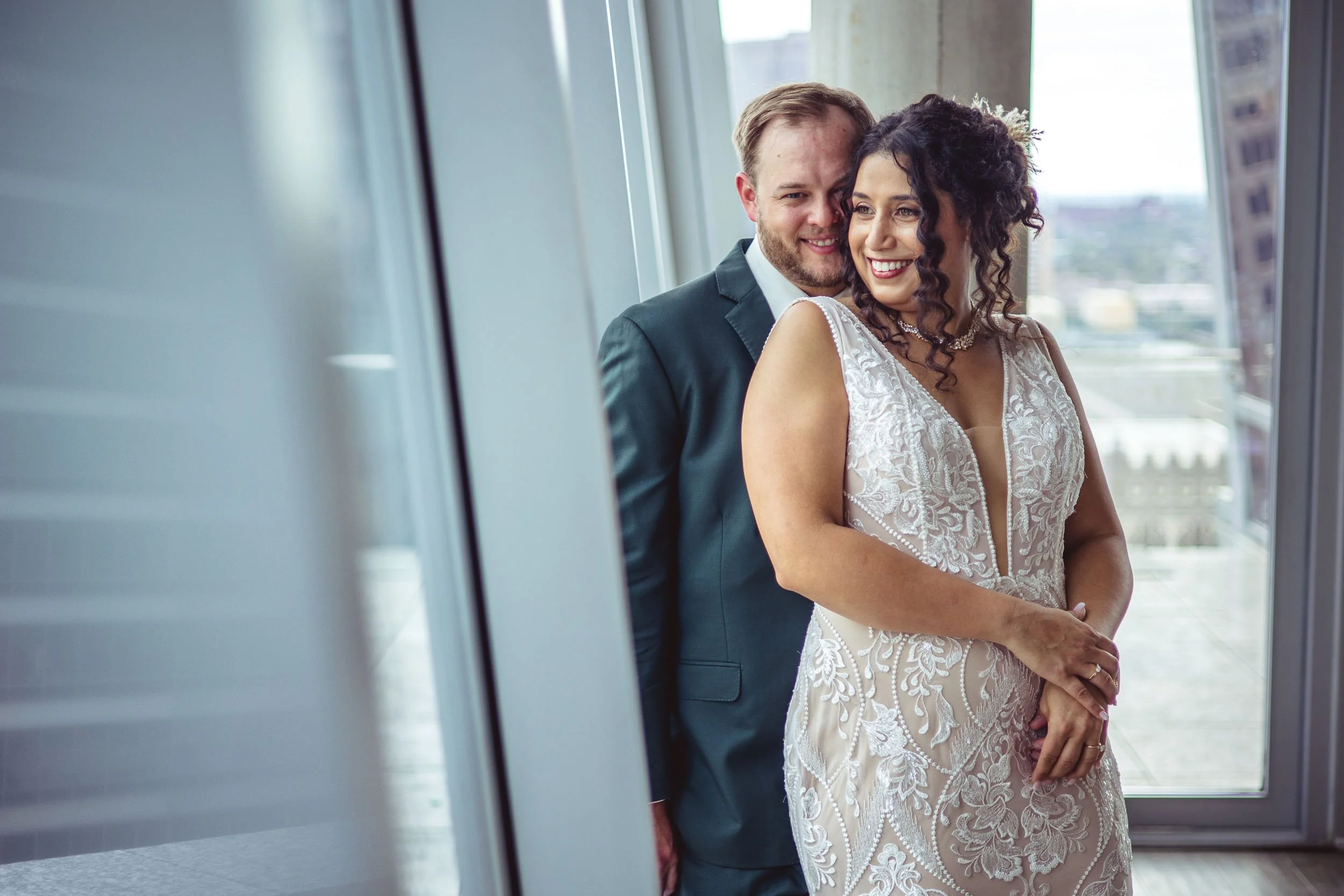 groom cuddles bride against a window overlooking the city of st louis