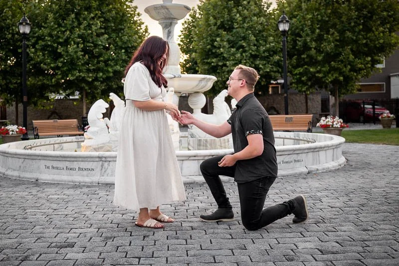 man proposing on one knee in front of a fountain