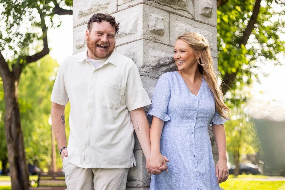 engaged couple holding hands and laughing against a pillar in tower grove park-st louis engagement photos