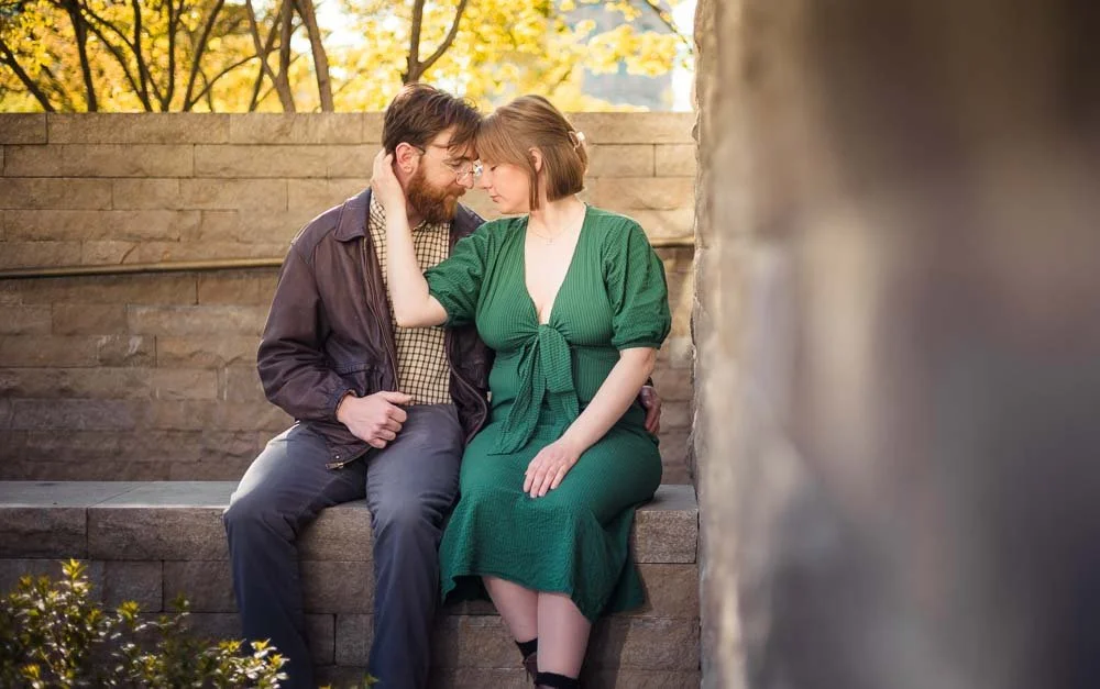 couple sitting on a wall holding each other lovingly-city garden engagement photos
