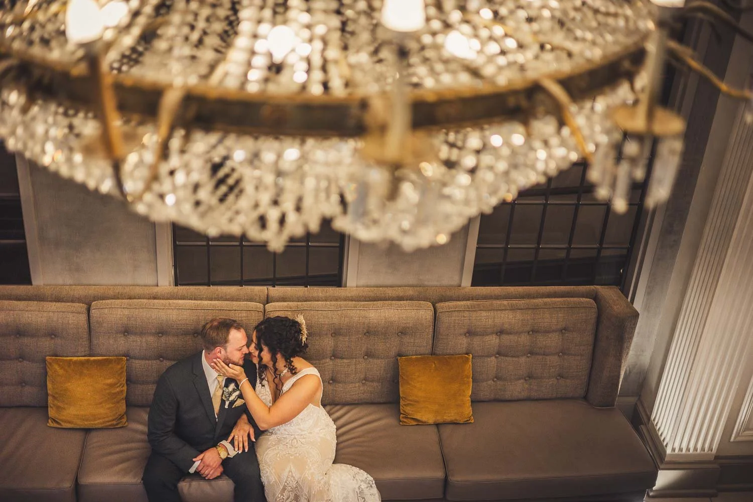 portrait of bride and groom sitting on a couch with a chandelier overhead