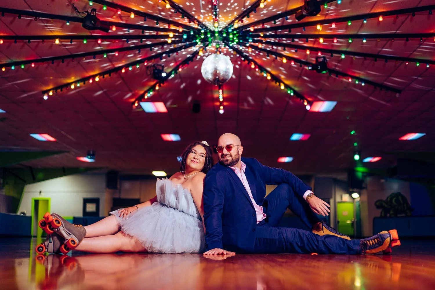 engaged couple sitting back to back on roller rink with skates on-arnold mo engagement photography