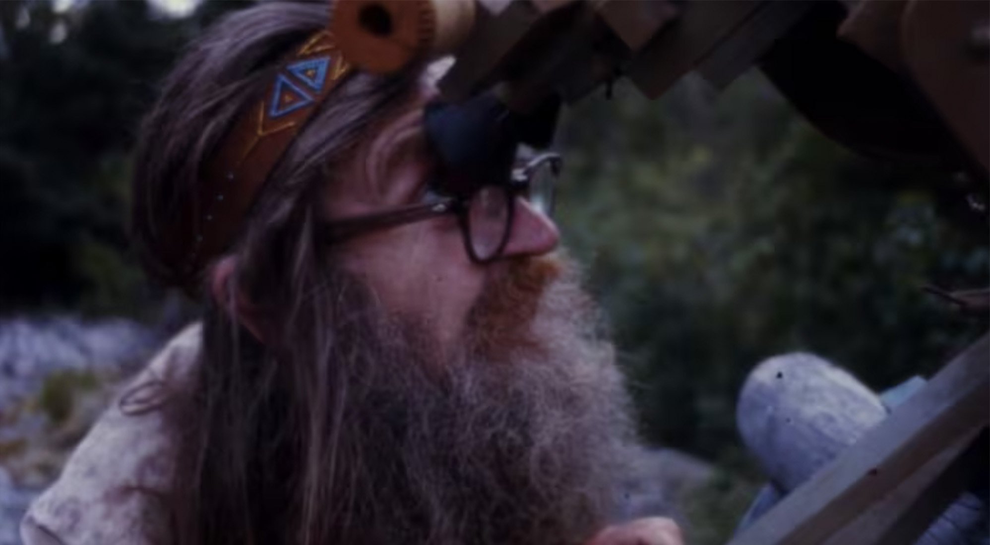 bearded Wendell looks over his glasses into the eye pieces of a handmade telescope