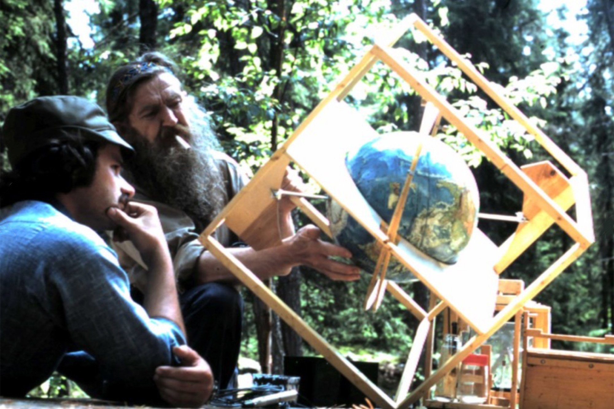 Old man Wendell with a cigarette in his mouth, a globe of the world inside a wooden contraption, a young man learning about the old man's theories