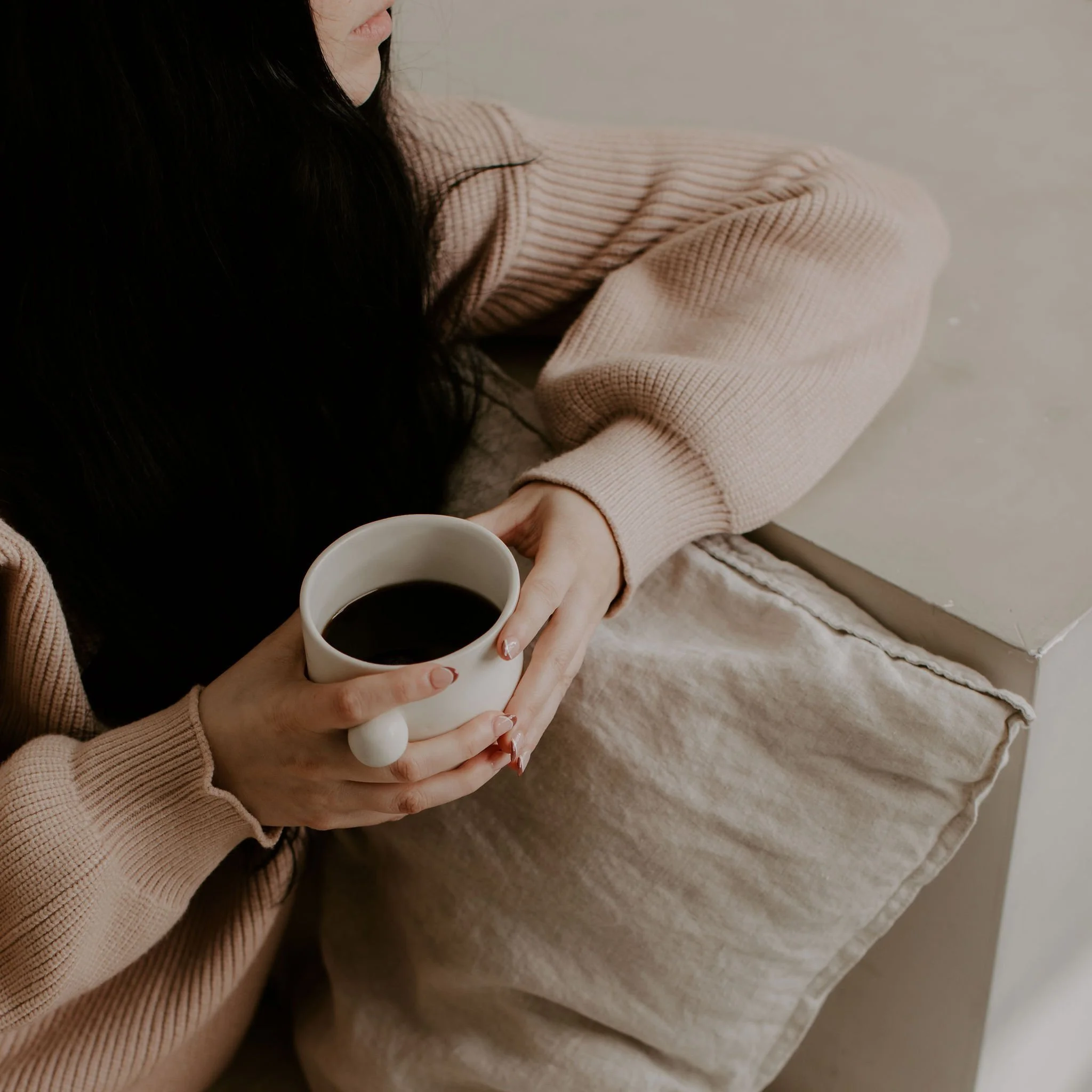 Woman holding cup of coffee with both hands on couch.