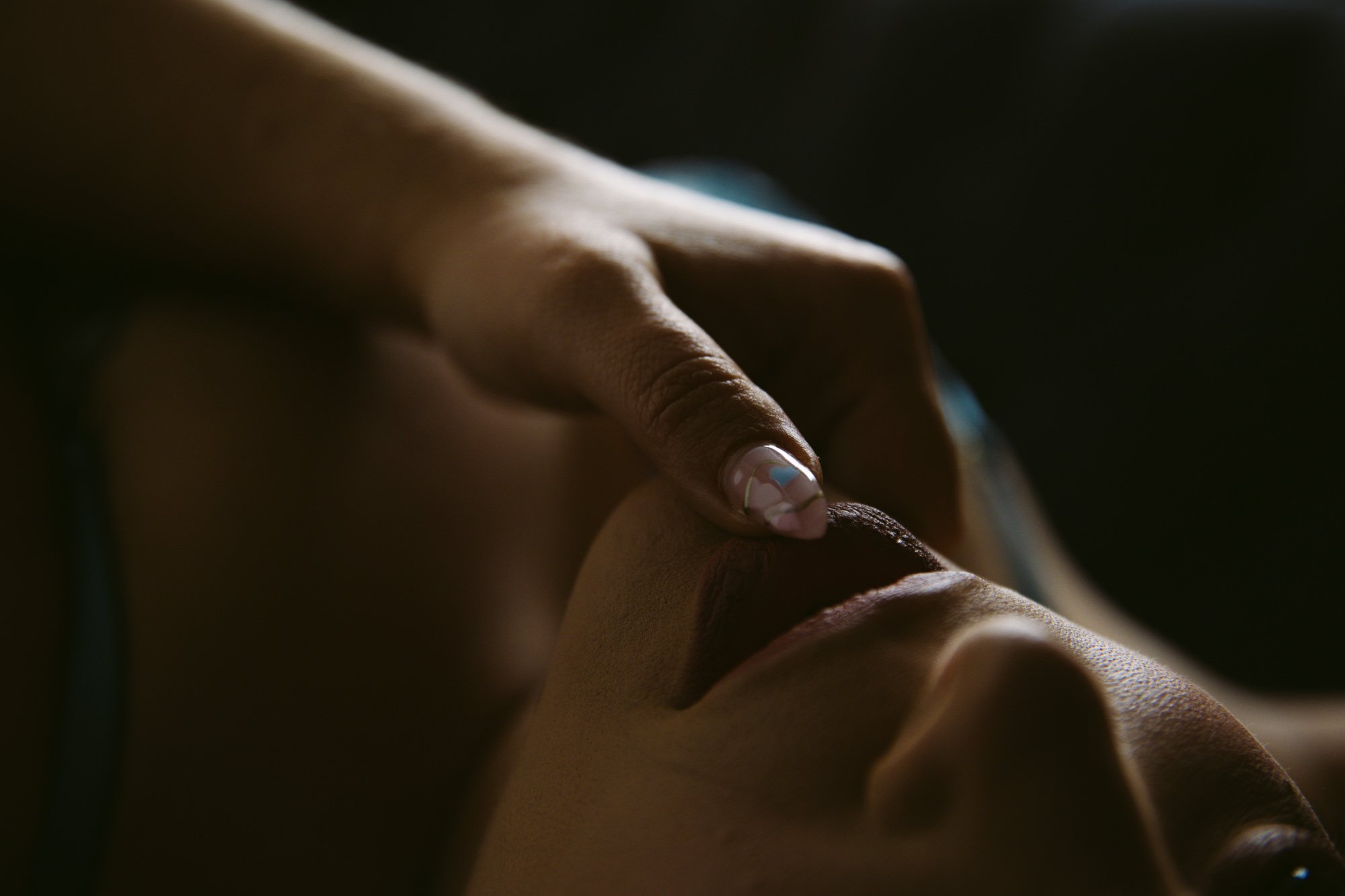 Close-up of a hand with a painted nail, touching a person's forehead.