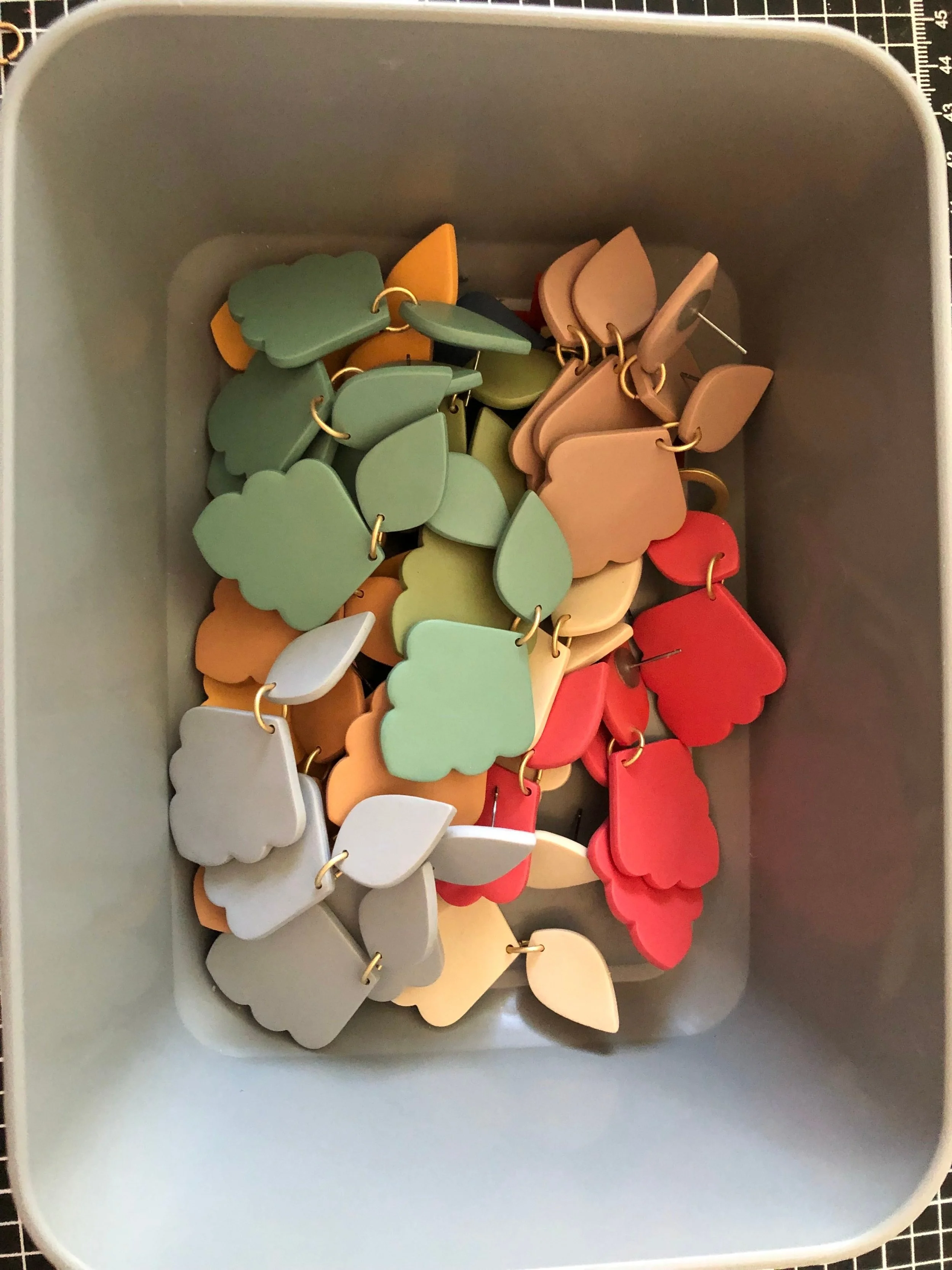 A collection of multicolored acrylic shapes connected by gold-tone rings, stored inside a light-colored storage bin.