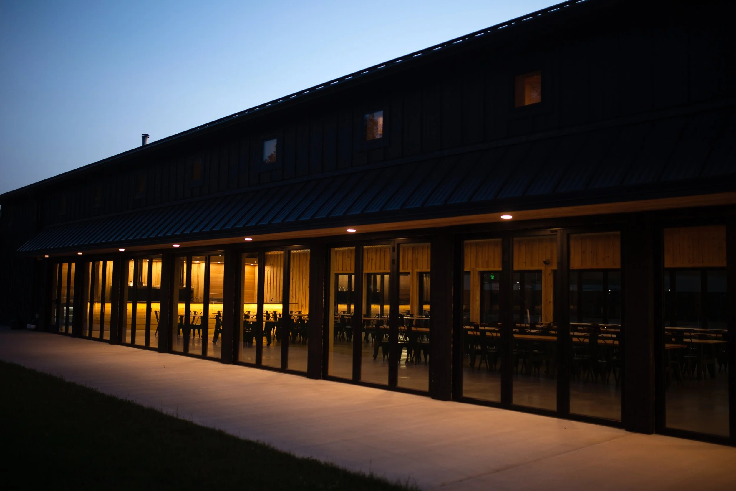 A modern building with large glass doors and windows, illuminated from inside, during dusk or nighttime.