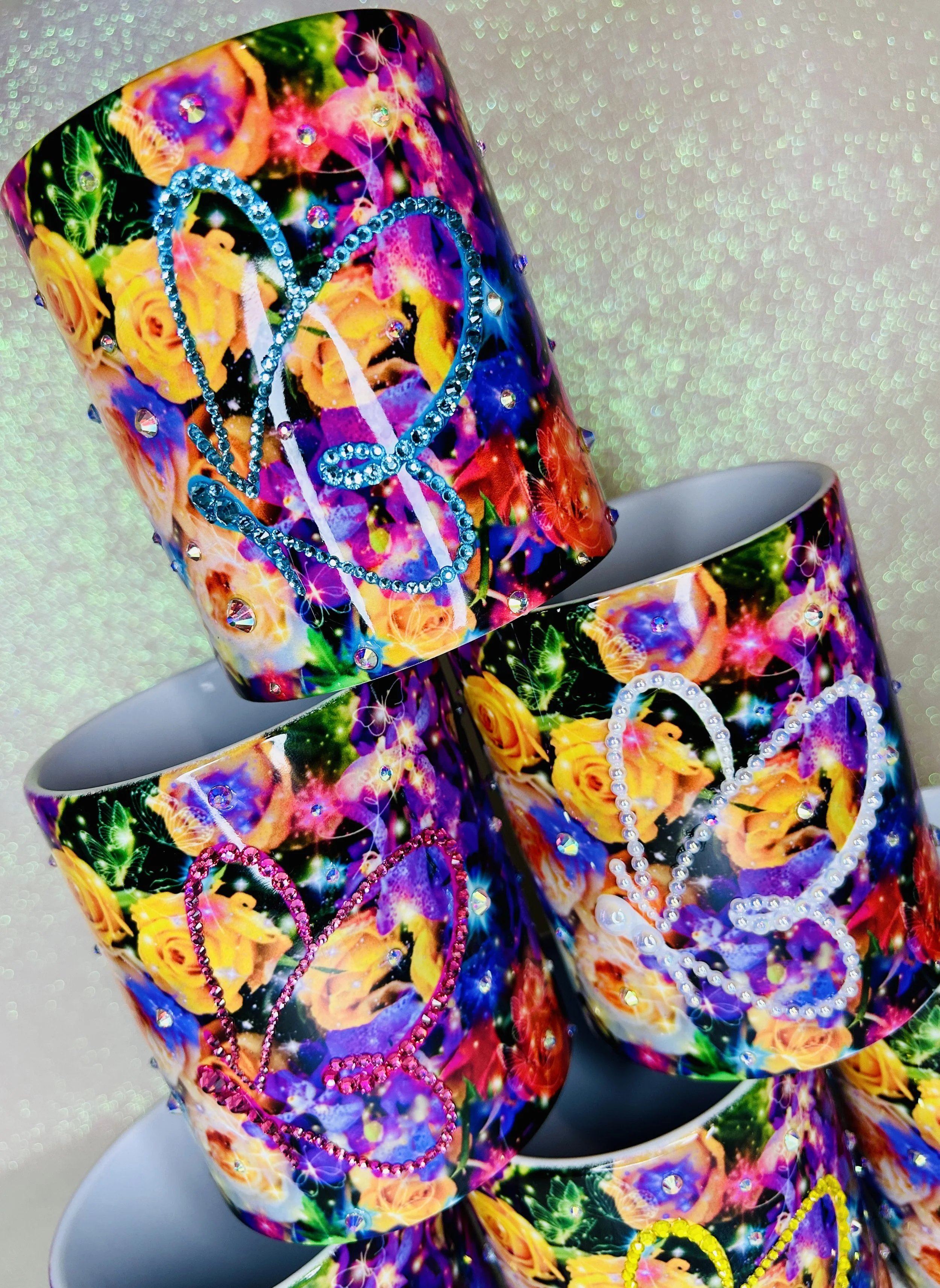 Colorful mugs with floral designs and rhinestone heart shapes stacked together.