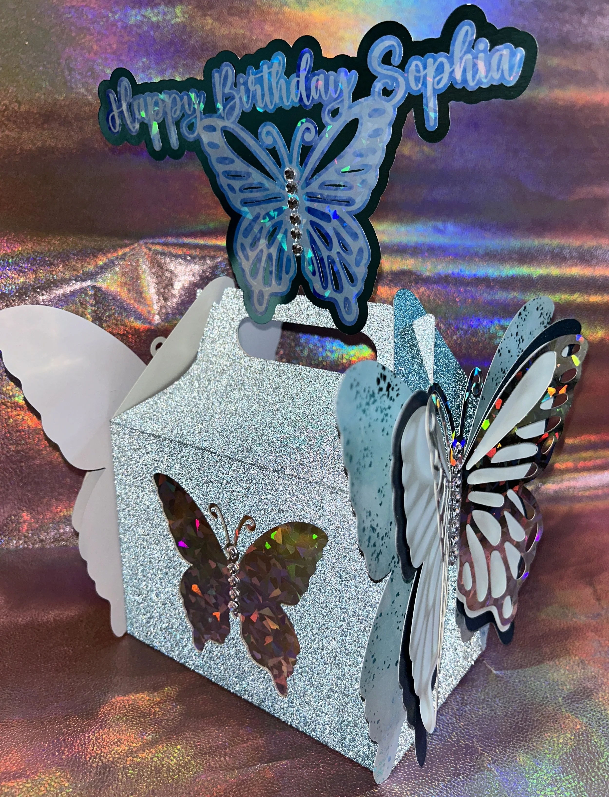 A glittery decorative box with a butterfly theme and "Happy Birthday Sophia" text on top.