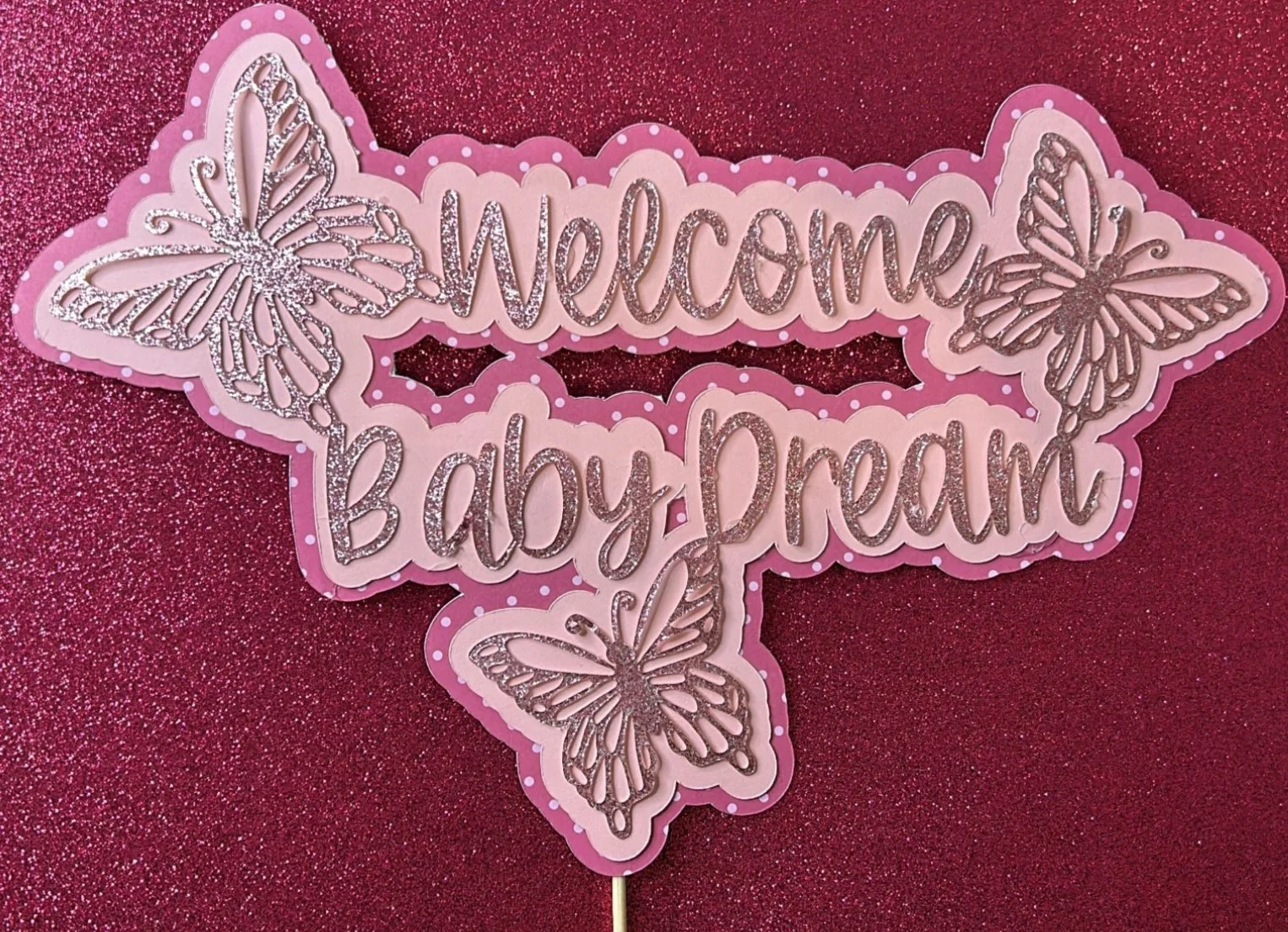 Glittery pink sign with "Welcome Baby Dream" text and butterfly decorations.