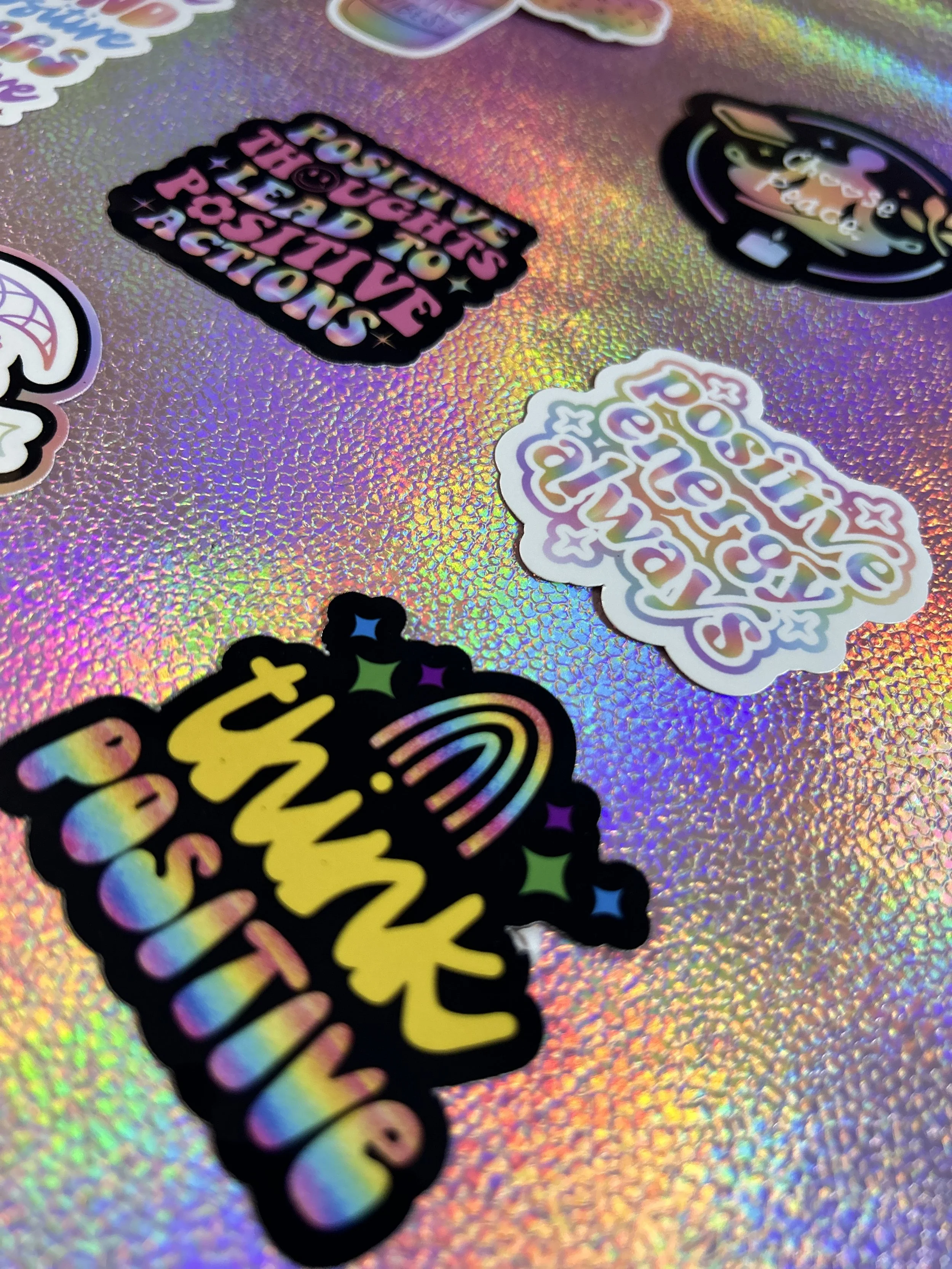 Various stickers with motivational phrases like "Think Positive" and "Positive Thoughts Lead to Positive Actions" on a holographic background.