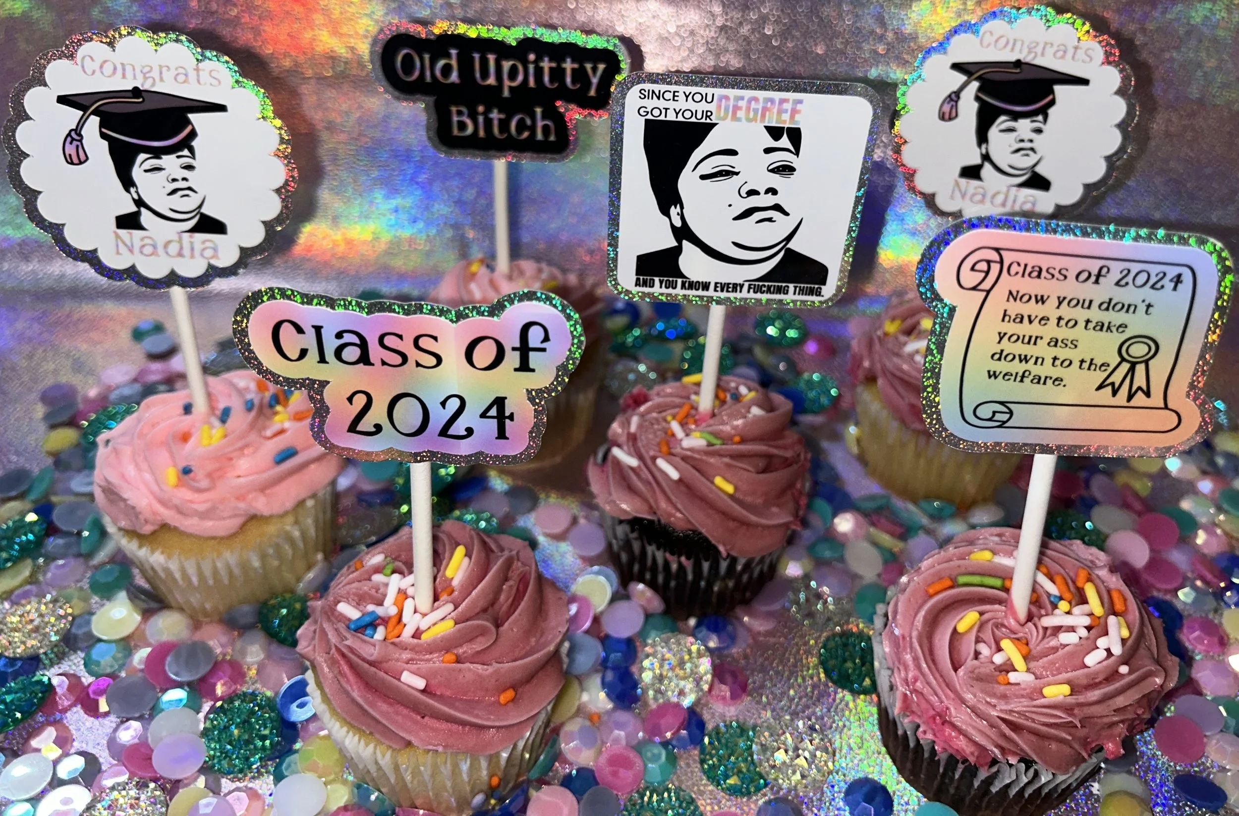 Cupcakes with colorful icing and sprinkles, topped with humorous graduation-themed toppers for the Class of 2024.