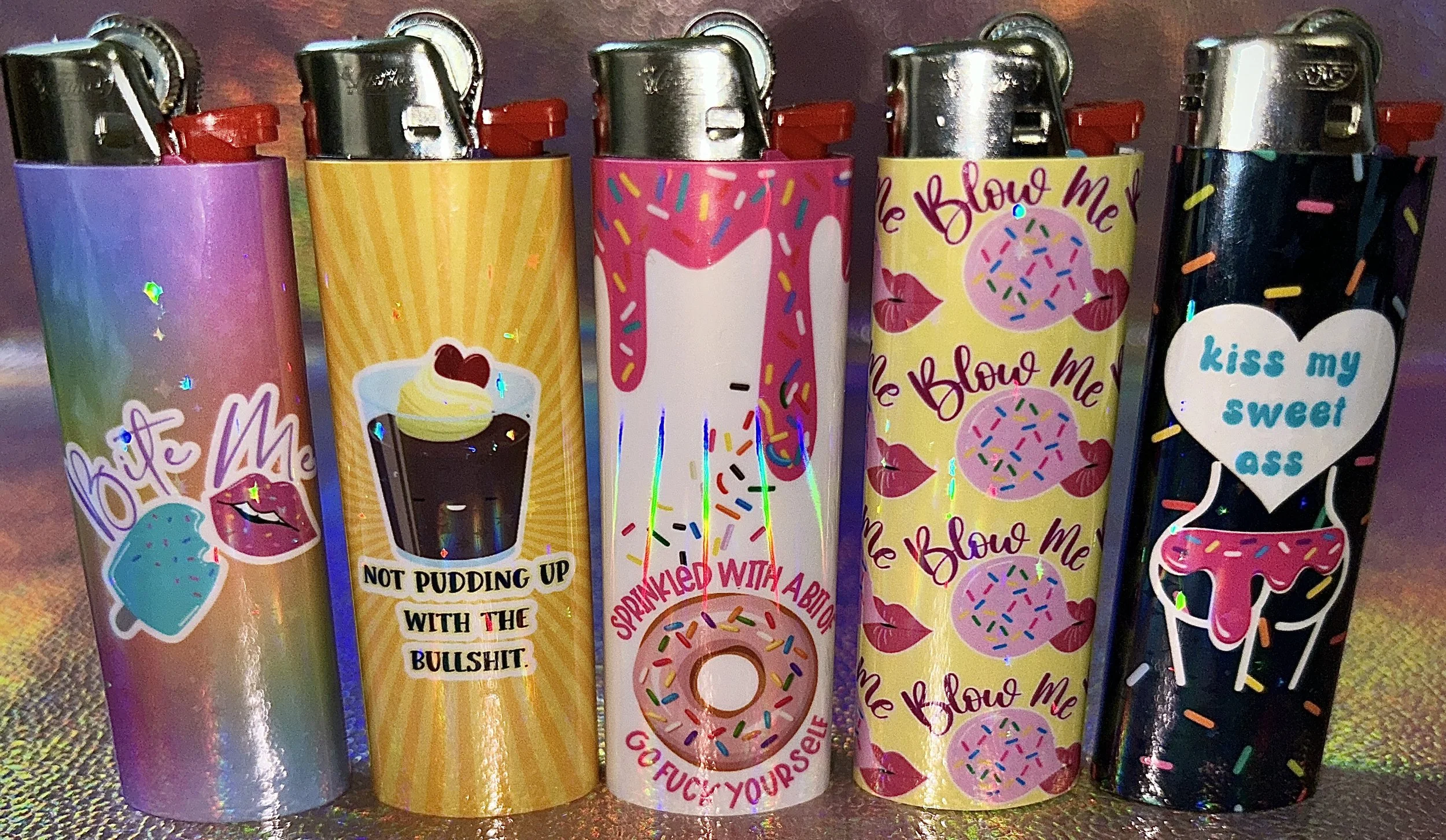 Five colorful cigarette lighters with humorous graphic designs and text, including images of desserts and playful phrases.