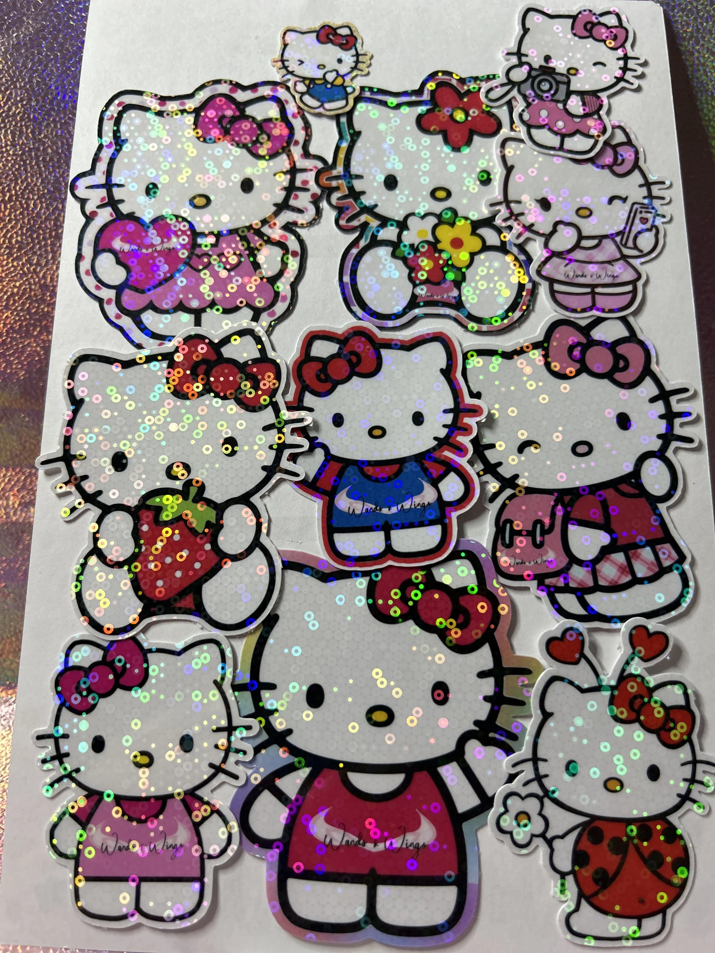 Holographic Hello Kitty stickers with various outfits and accessories on a sheet.