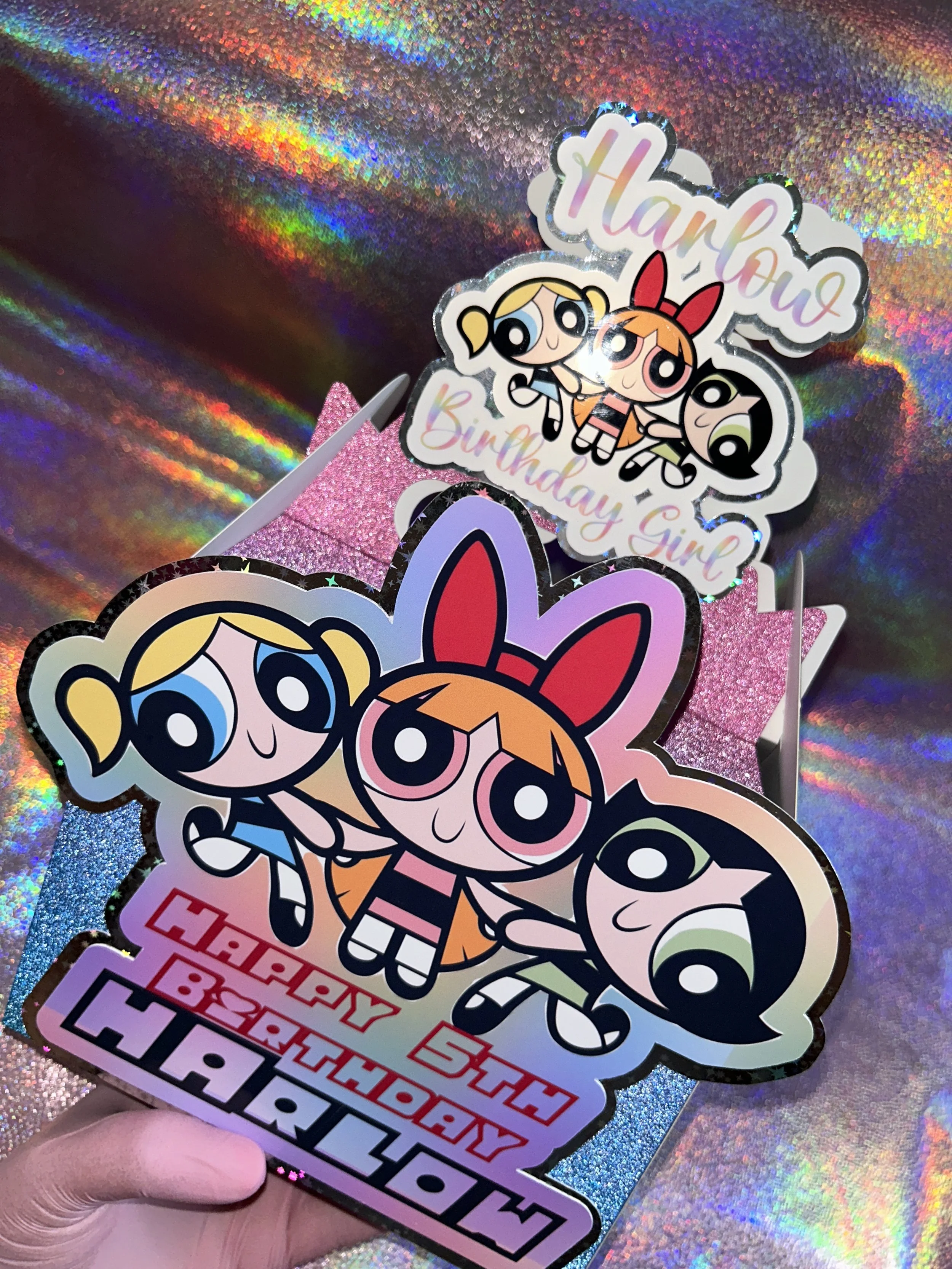 Powerpuff Girls themed birthday decorations on a holographic background, featuring a cutout with "Happy 5th Birthday Harlow" text and images of the characters Blossom, Bubbles, and Buttercup.