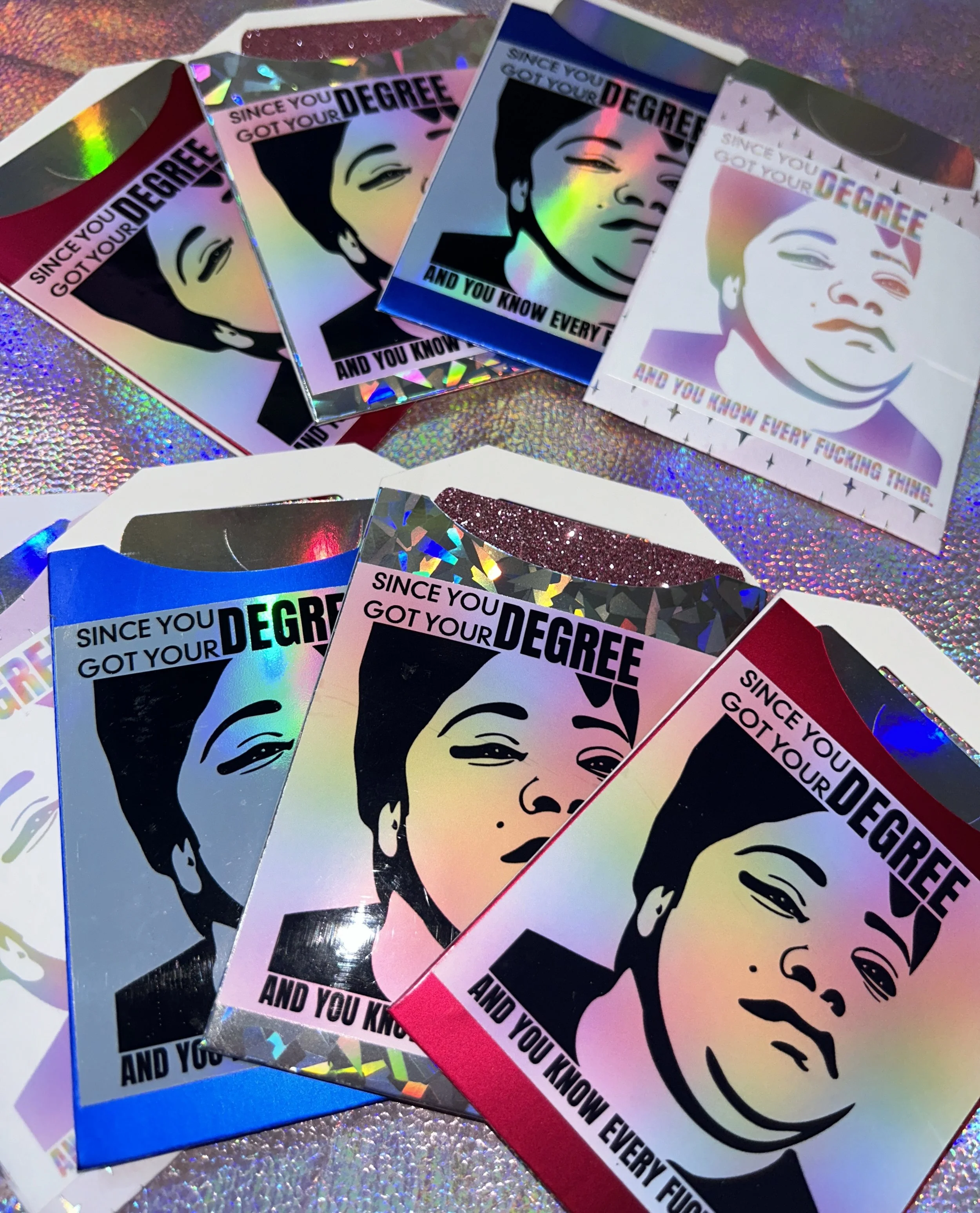 A collection of holographic stickers, each featuring an artistic portrait and the text 'Since you got your degree and you know everything.' The stickers vary in color and texture, spread out on a glittery background.