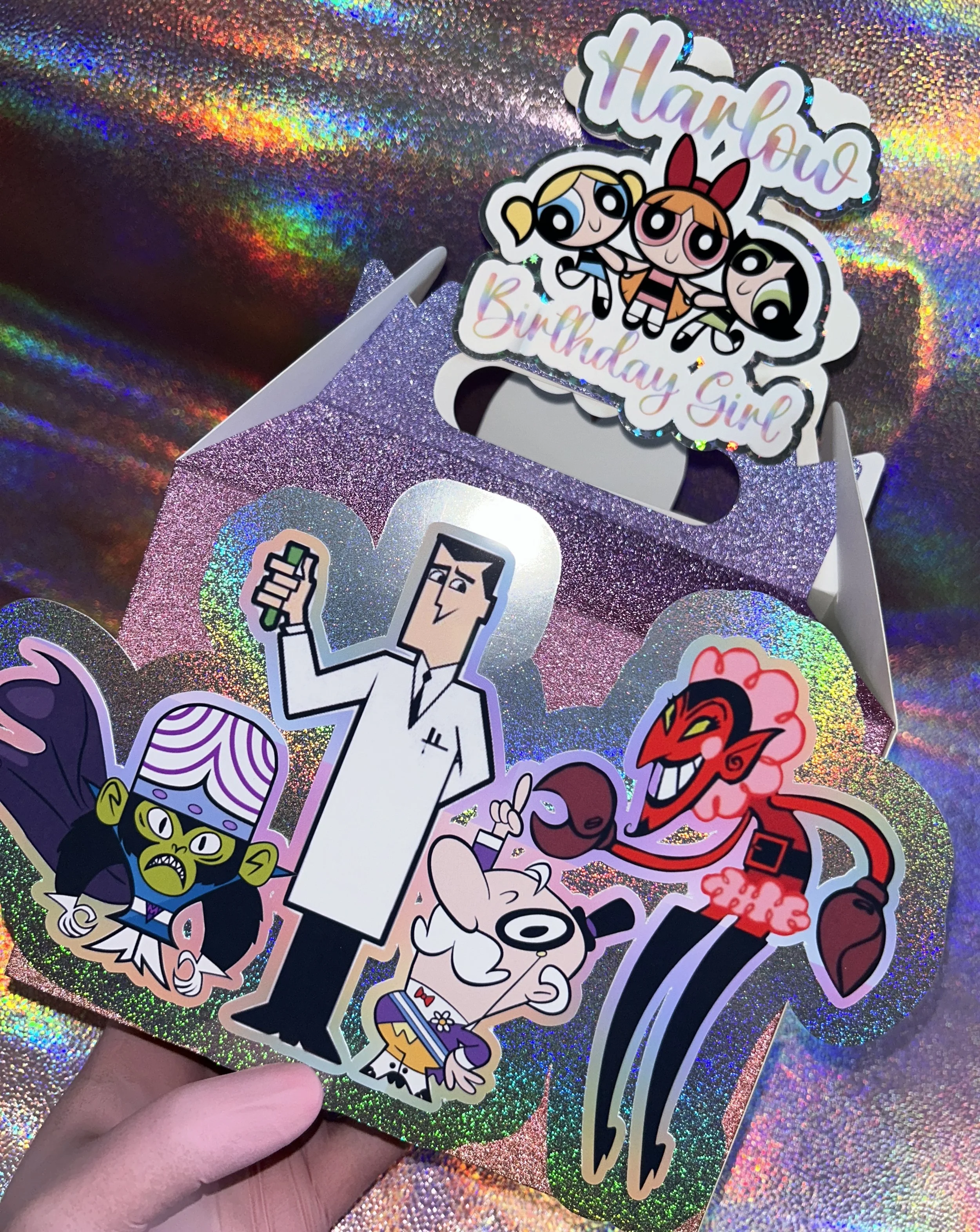 A holographic birthday card featuring cartoon characters from "The Powerpuff Girls." Characters include Mojo Jojo, Professor Utonium, and others. The card is personalized with the name "Harlow" and the words "Birthday Girl".
