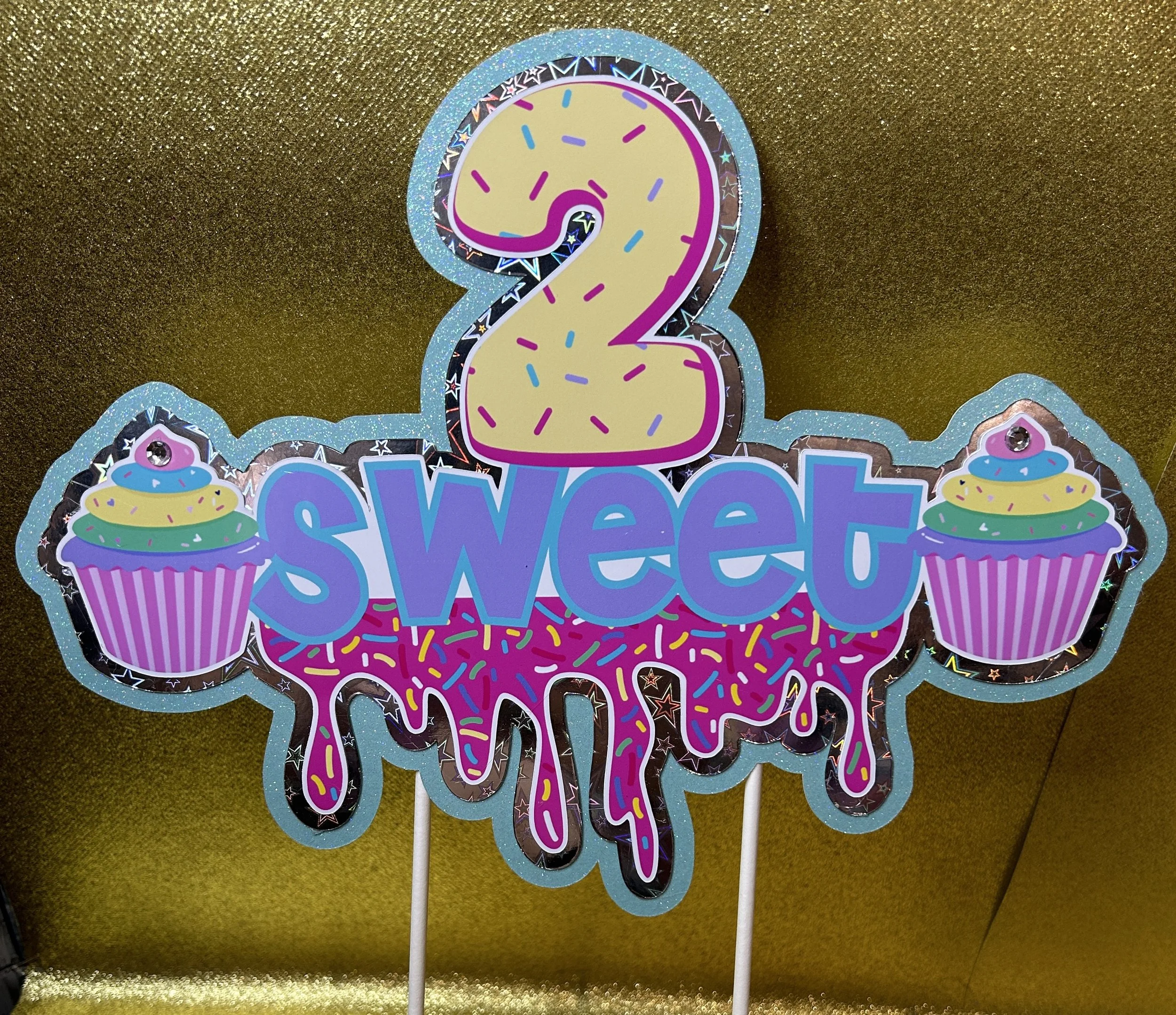 "2 sweet" birthday decoration with cupcakes on a glittery gold background.