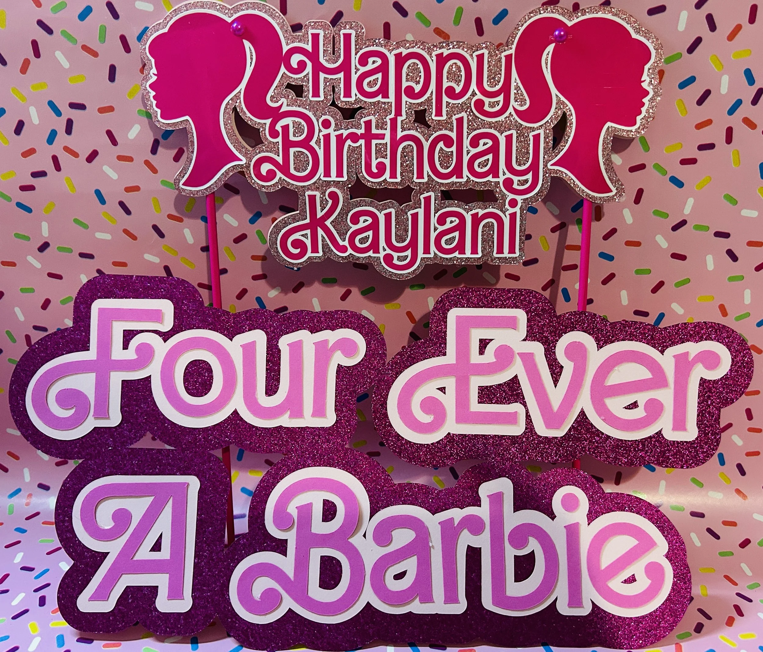 Birthday cake topper with text "Happy Birthday Kaylani" and "Four Ever A Barbie" on a sprinkle-patterned background.