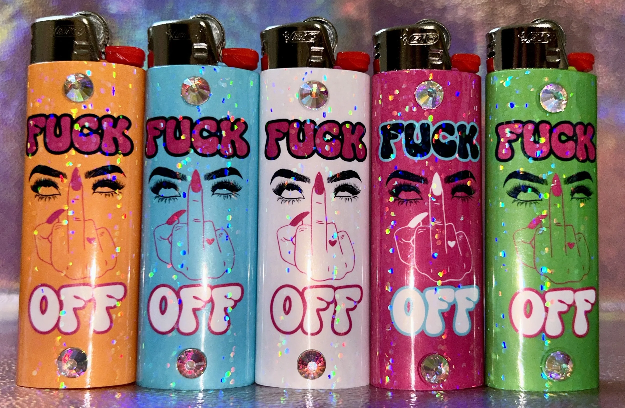 Five colorful lighters with a middle finger graphic and text saying "F**k Off," adorned with sparkly embellishments.