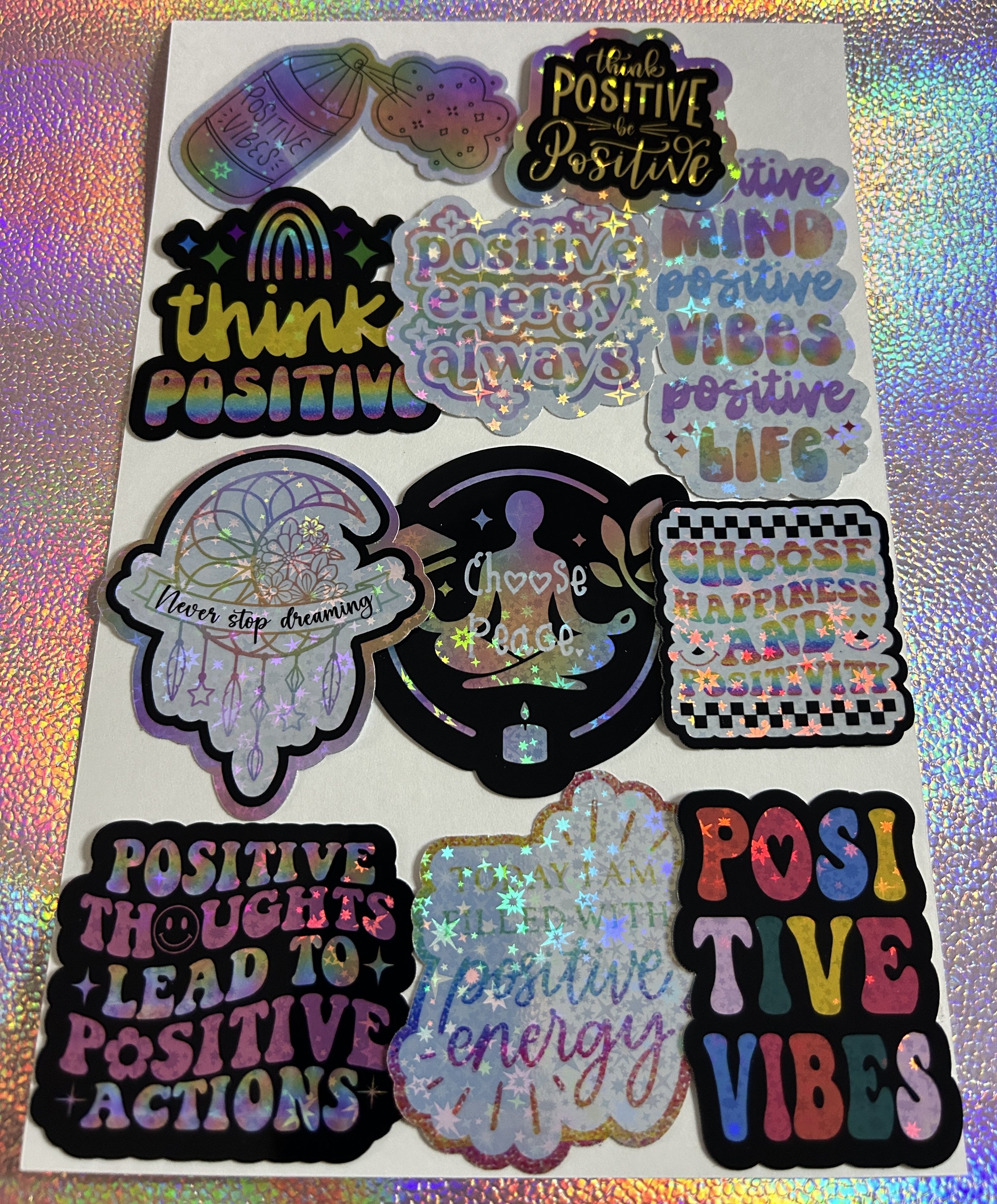 A collection of colorful, motivational stickers with phrases like "Positive Vibes," "Think Positive," "Positive Energy Always," "Choose Peace," and "Positive Thoughts Lead to Positive Actions." The stickers have a holographic effect, emphasizing posi