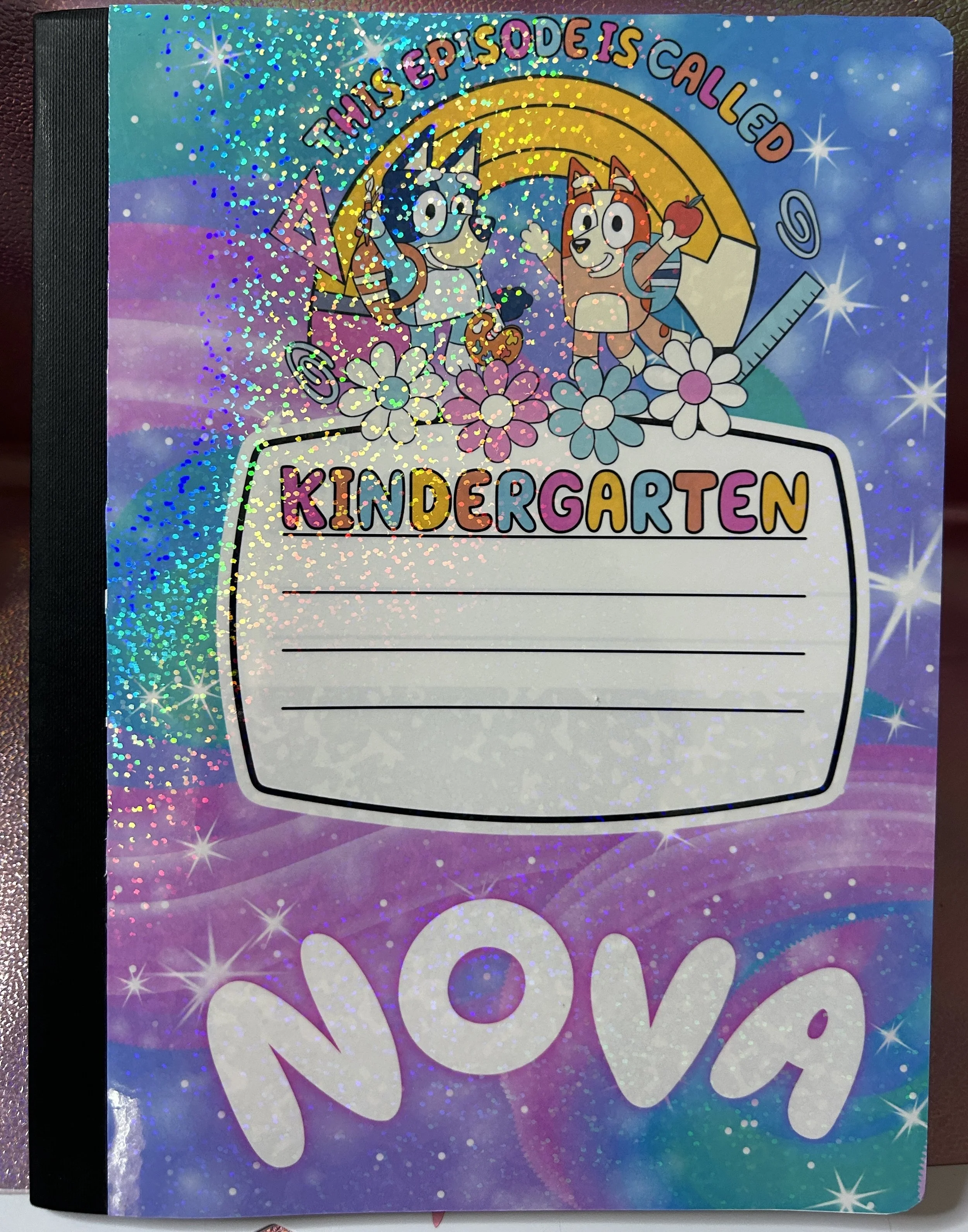 Colorful glittery children's notebook cover with cartoon dogs, "Kindergarten" label, and the name "Nova."