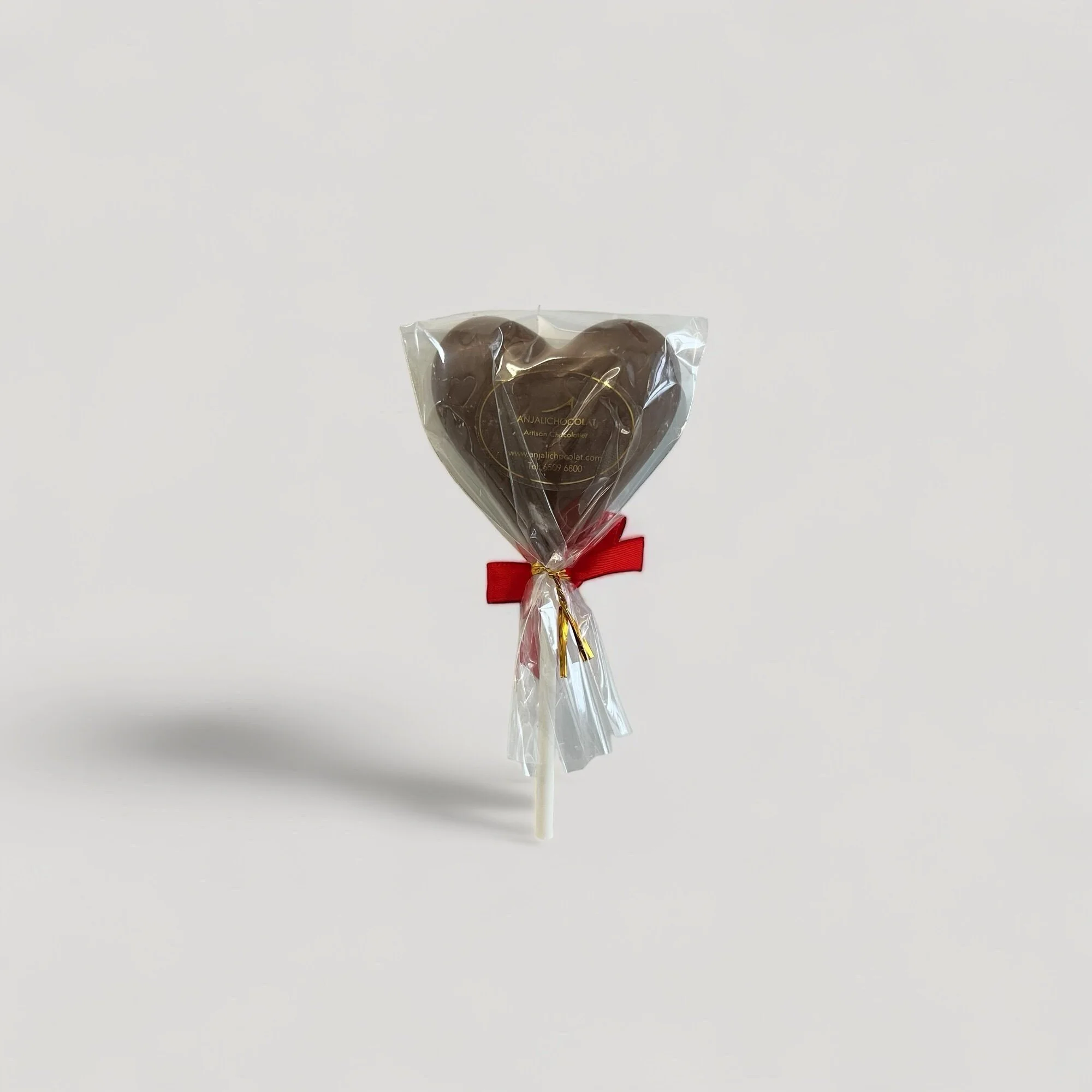 One heart-shaped lollipop in white chocolate with a red ribbon on a light grey background. A sweet treat for Valentine's Day or any occasion