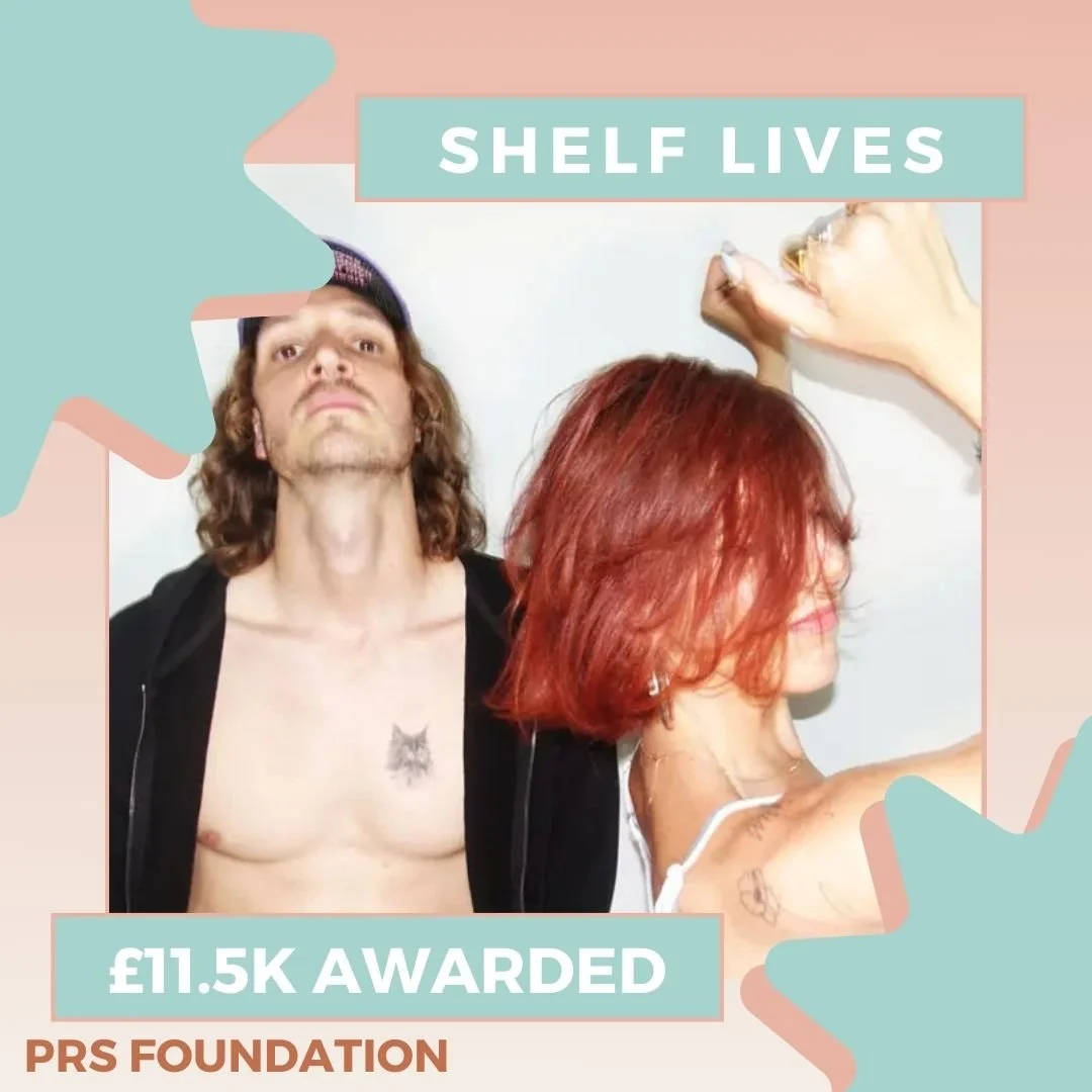 Young man in the background standing facing the camera, a young woman with short red hair standing sideways with arms raised. Blue and pink graphics, text reads: Shelf Lives, £11.5k awarded, PRS Foundation.