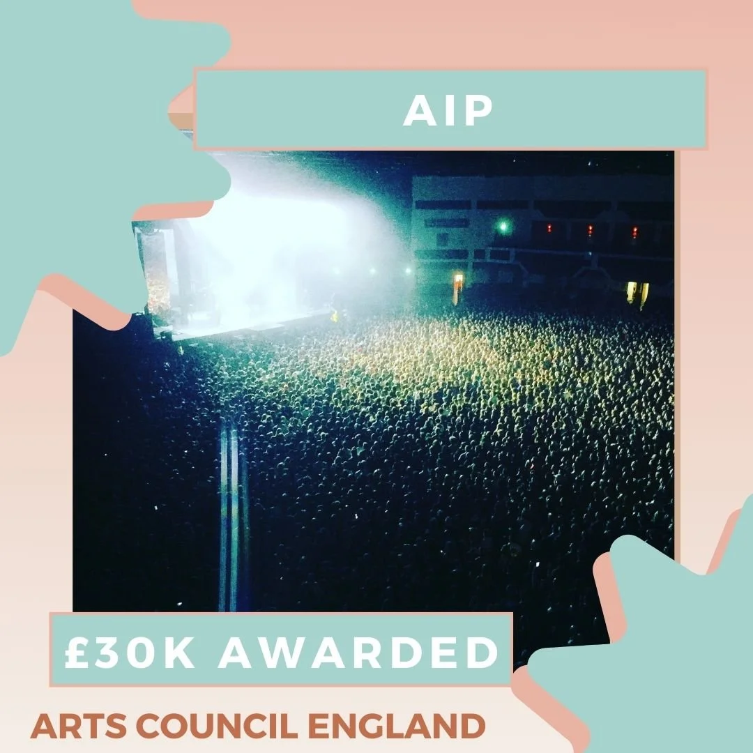 Overhead shot of a sold out crowd in front of a stage lit up with bright white lights. Text says: AIP, £30k awarded, Arts Council England.