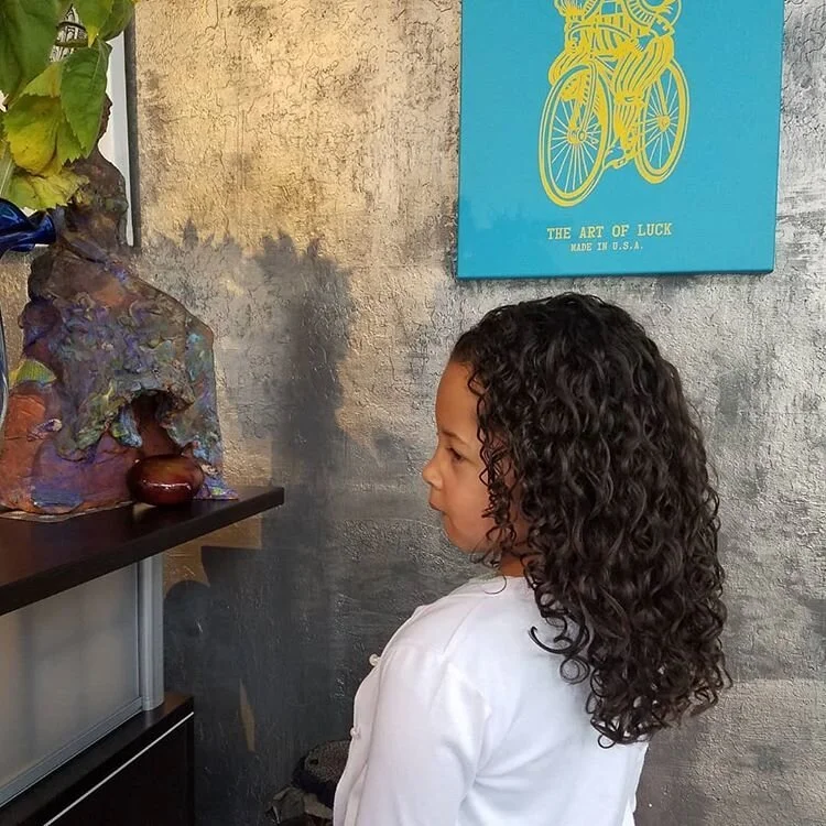 Young girl with curly hair looking at an art display on a textured wall.
