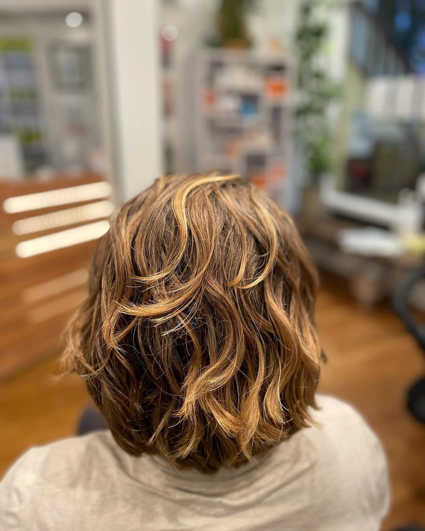 Back of a person's head with short, wavy, blonde and light brown hair in a salon setting.