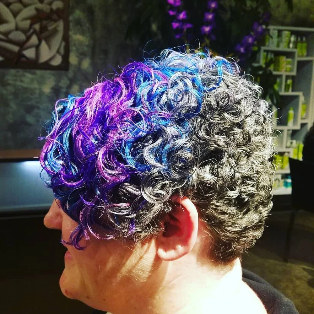 A person with short curly gray hair with vibrant purple and blue highlights.