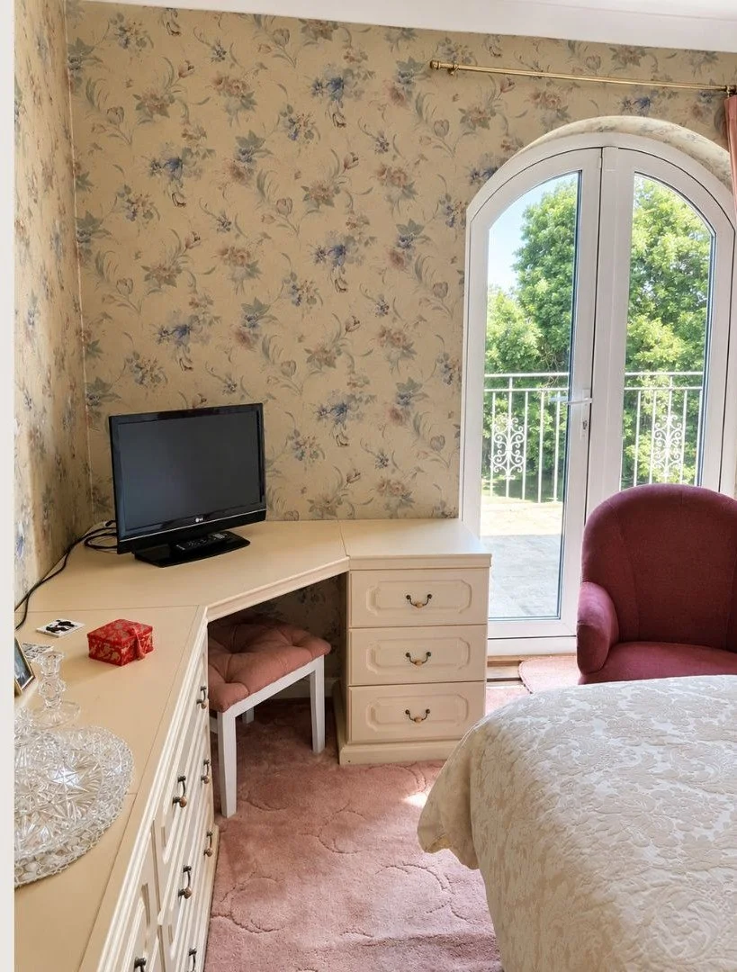 Original bedroom with corner dressing table, floral wallpaper and arched balcony doors.