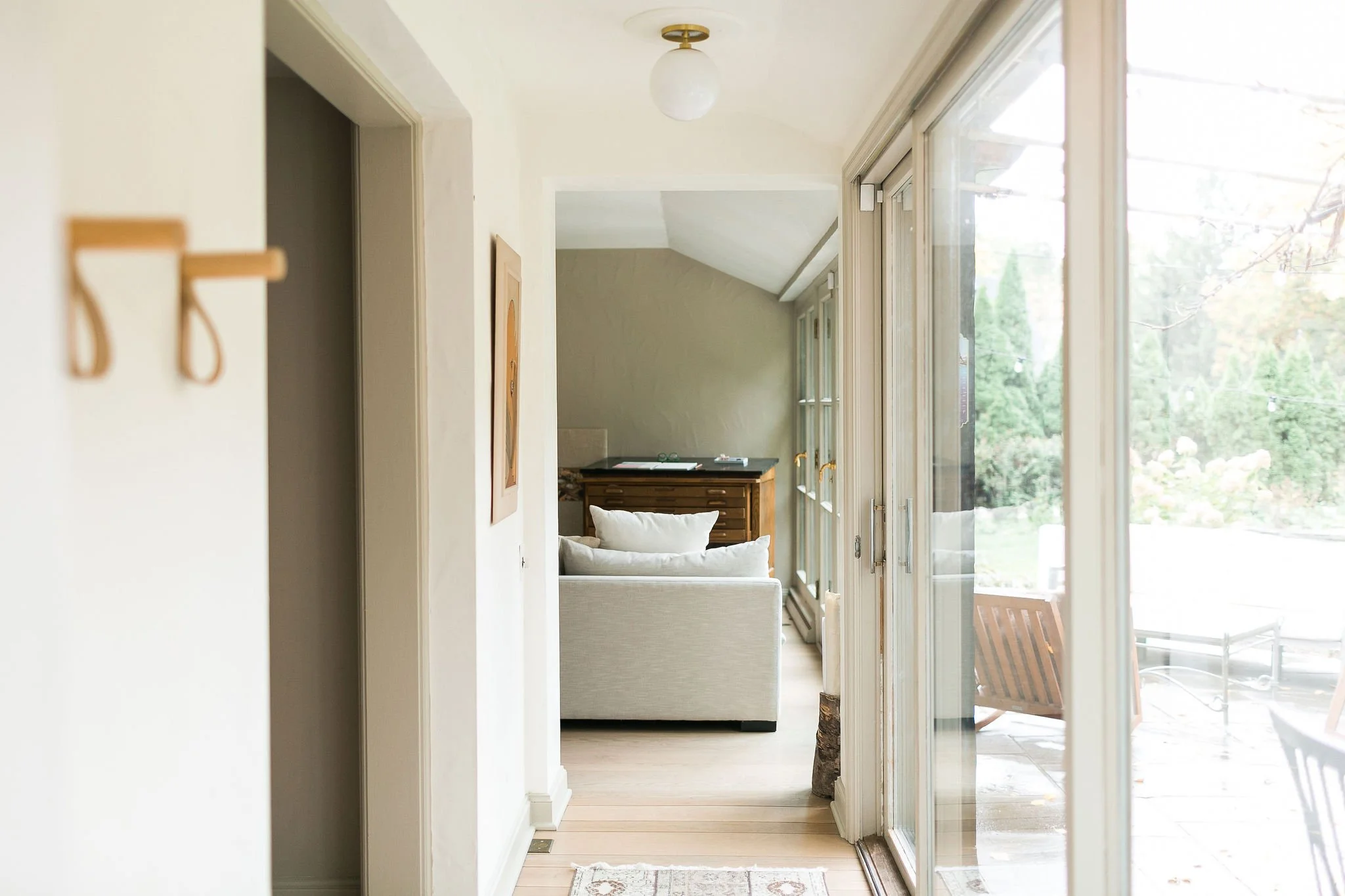 Bright living room with sliding glass door leading to outdoor patio, white sofa, wooden dresser, and natural light from windows.