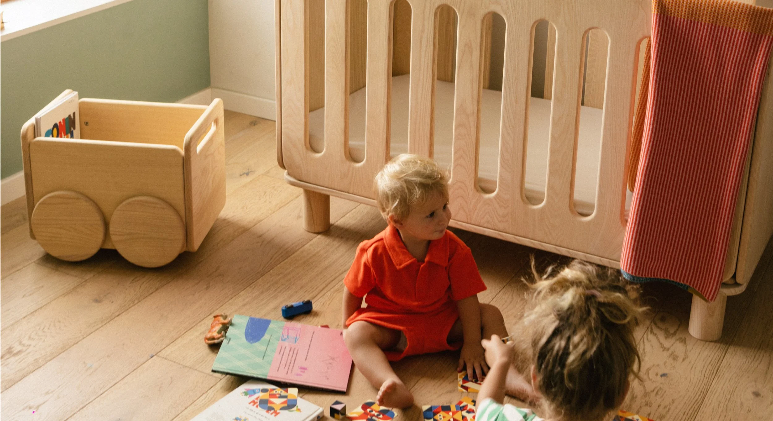 A young child playing in a nursery setting with the Kokozi cot and Olaki trolley, illustrating the integration of the collection into family life.