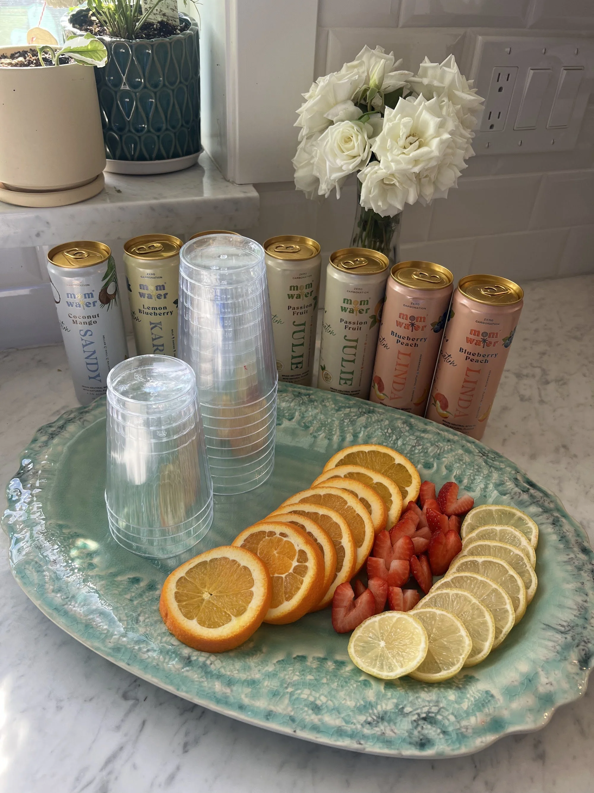 Mom Water cans lined up beside a fresh citrus and strawberry platter, UGC content by Homemade Social for Mom Water