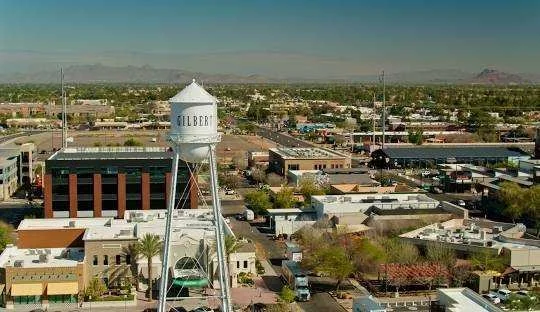 Cityscape with water tower labeled 'GILBERT' in Gilbert, Arizona, featuring various commercial buildings, trees, and a clear sky.