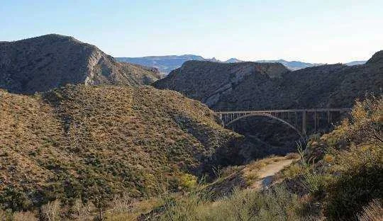 A scenic view of rugged hills and mountains with a bridge arching over a valley.
