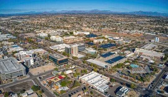 Aerial view of an urban area with various buildings, streets, and some open spaces, with a distant mountain range on the horizon.