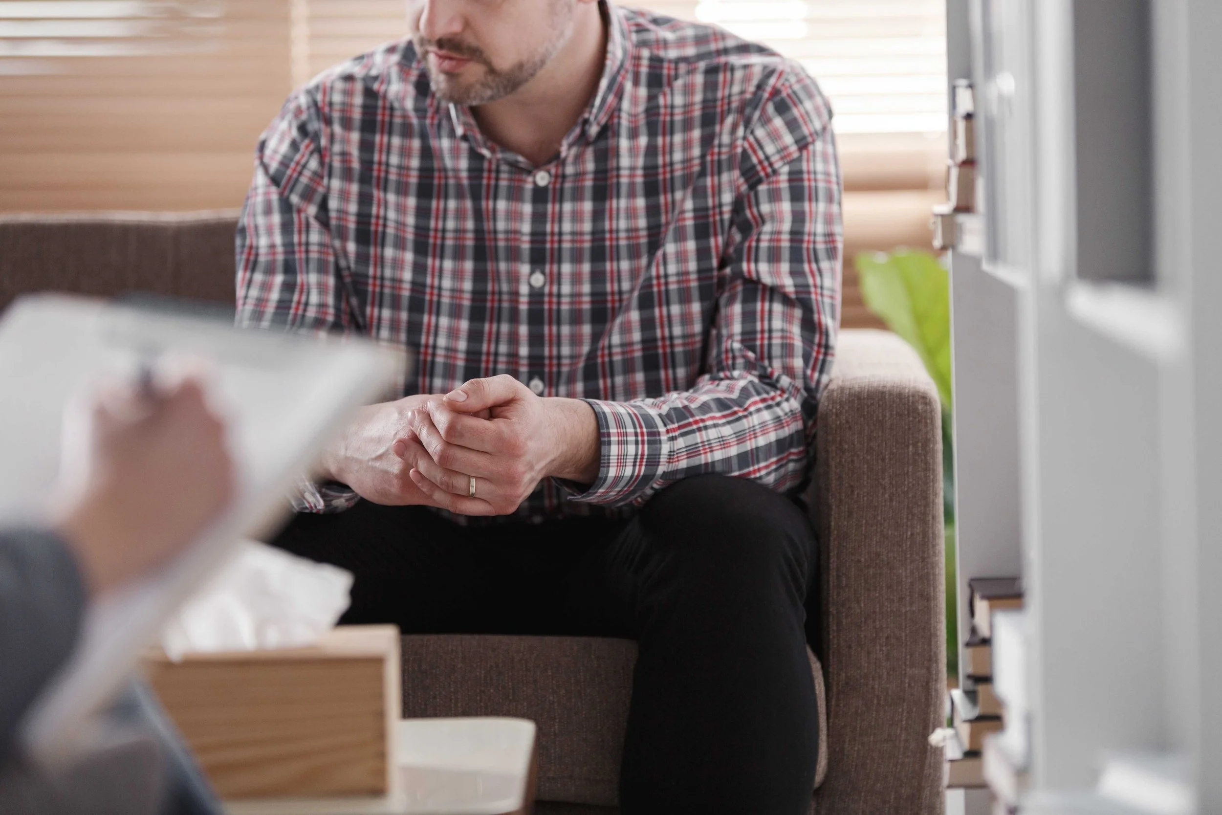 Man sitting with clasped hands in a coaching session, listening attentively in a calm, private setting