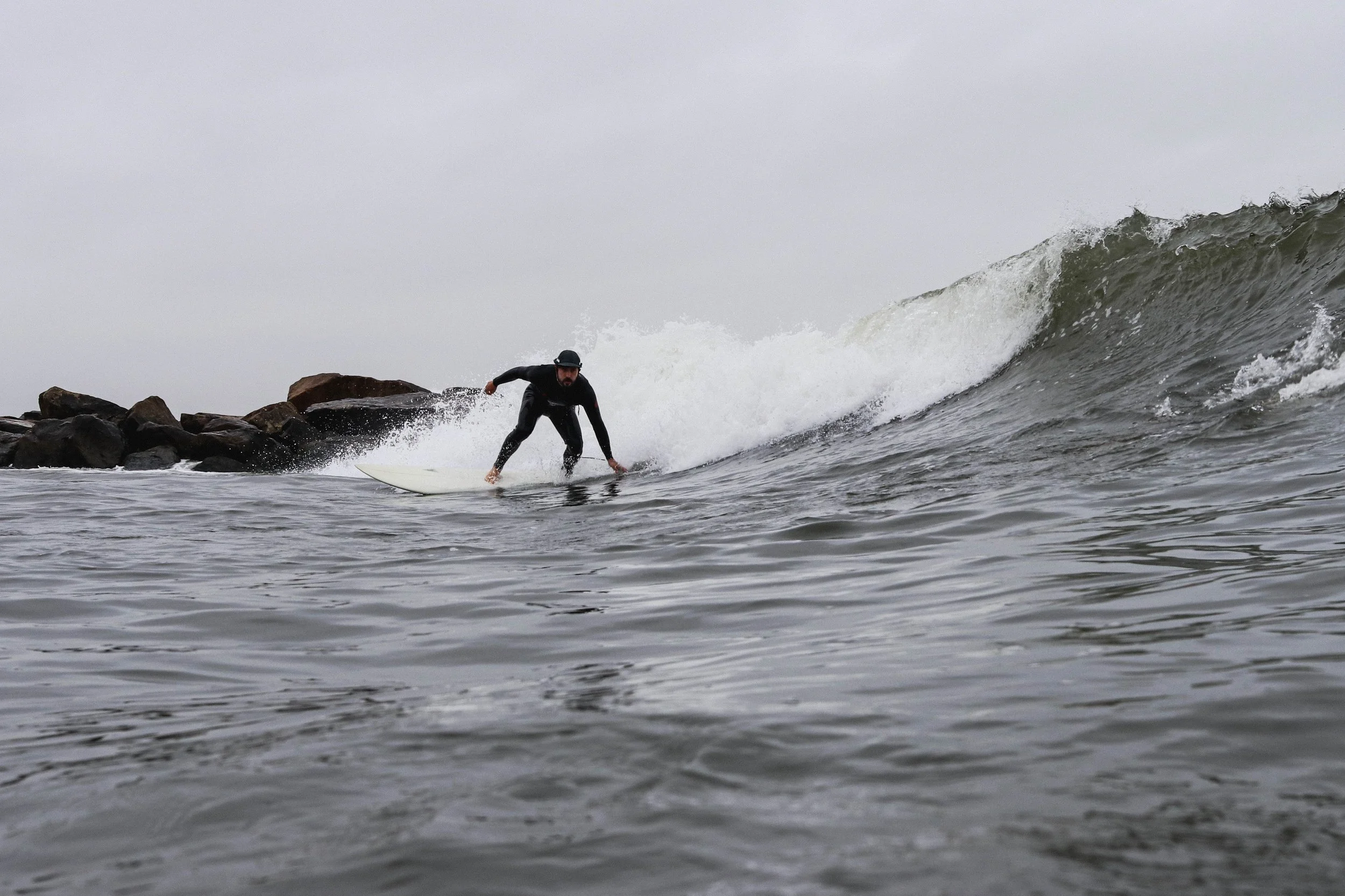 Person surfing on a wave near rocks under overcast sky.