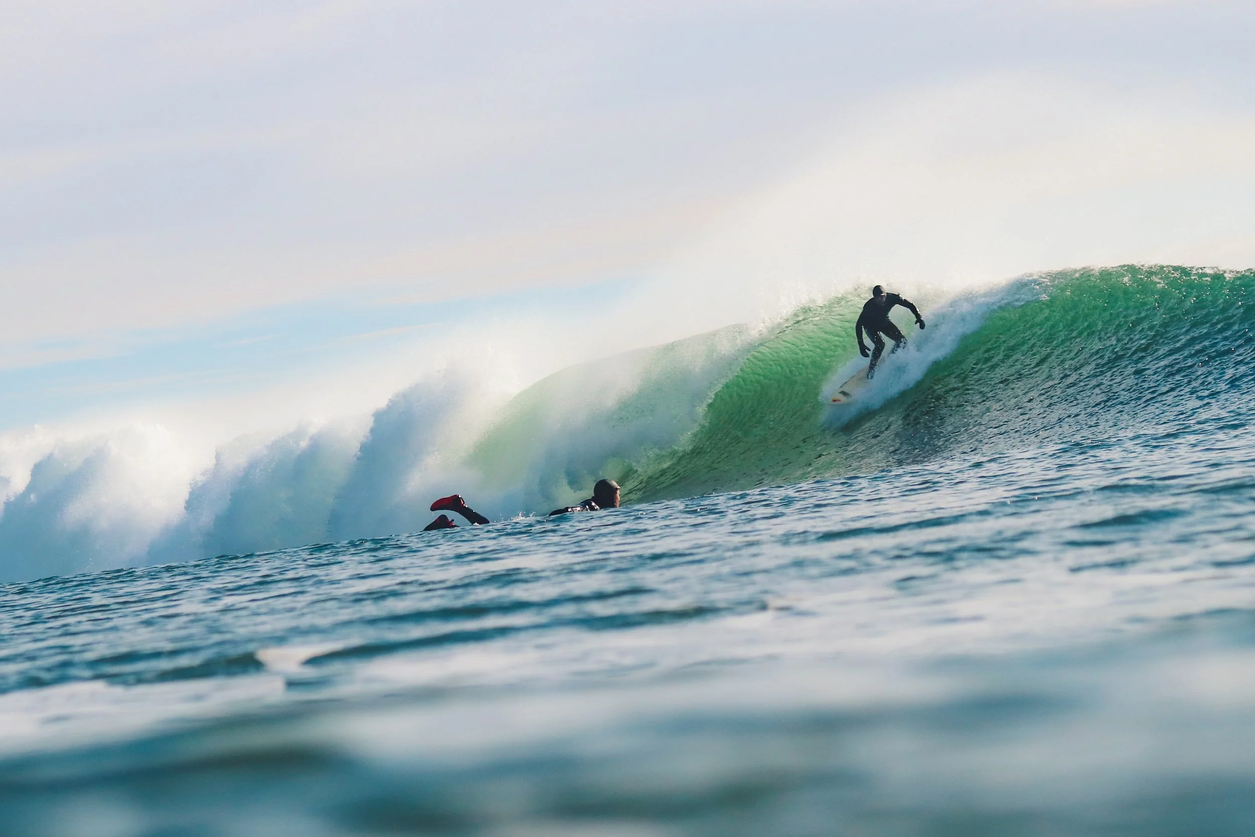 A surfer riding a large wave while two other surfers are in the water watching from below.