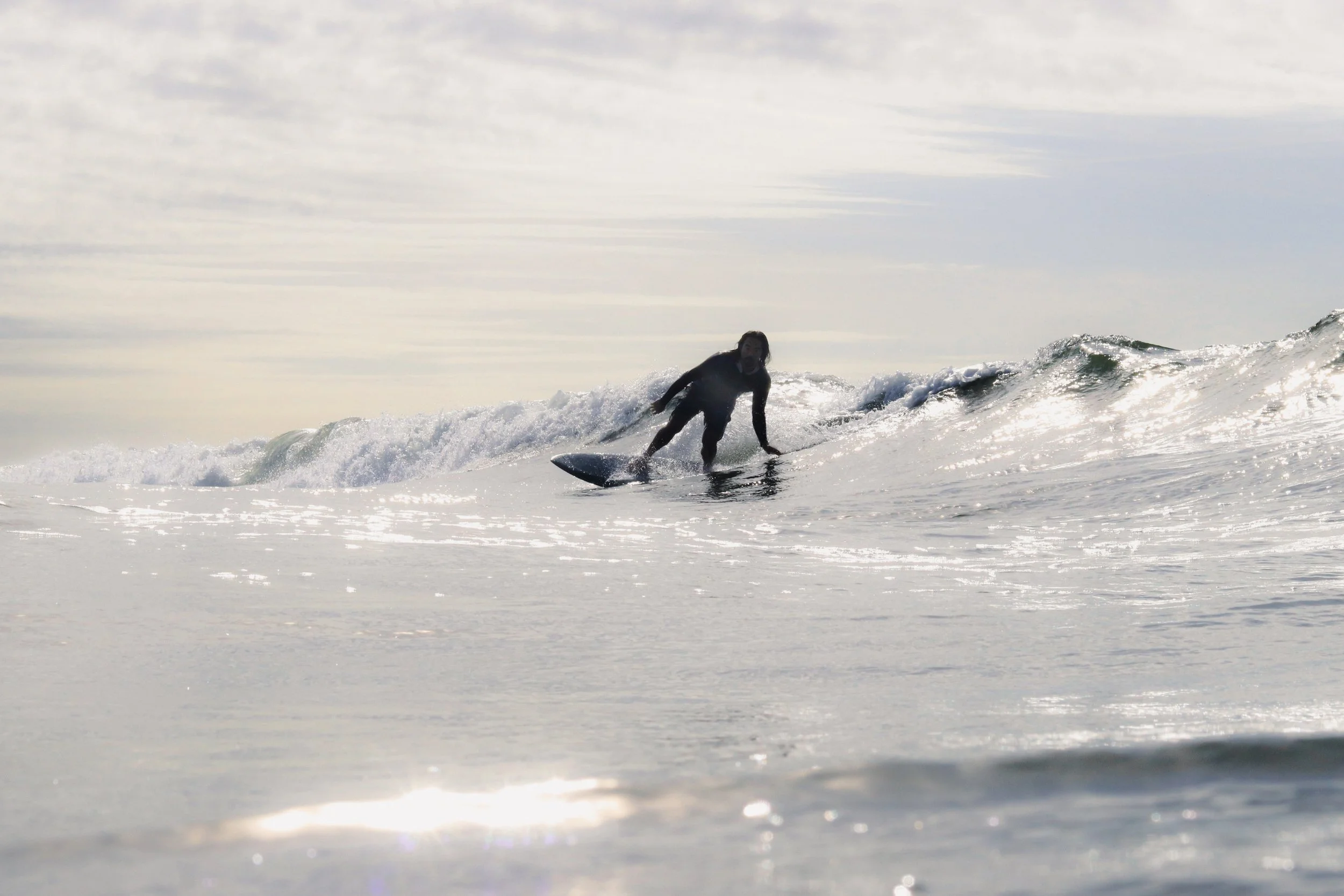 A person surfing on a wave in the ocean with a cloudy sky above.