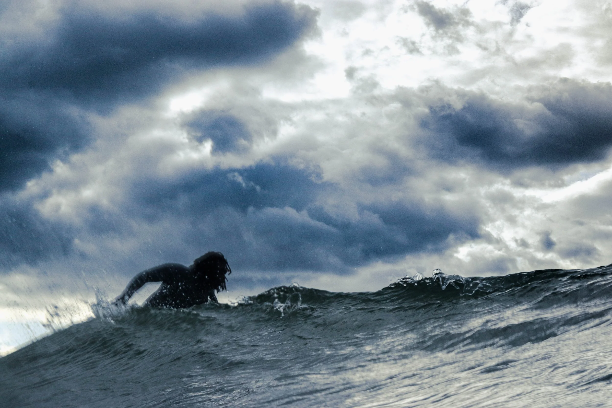 A person swimming in the ocean with a stormy sky and dark clouds overhead.